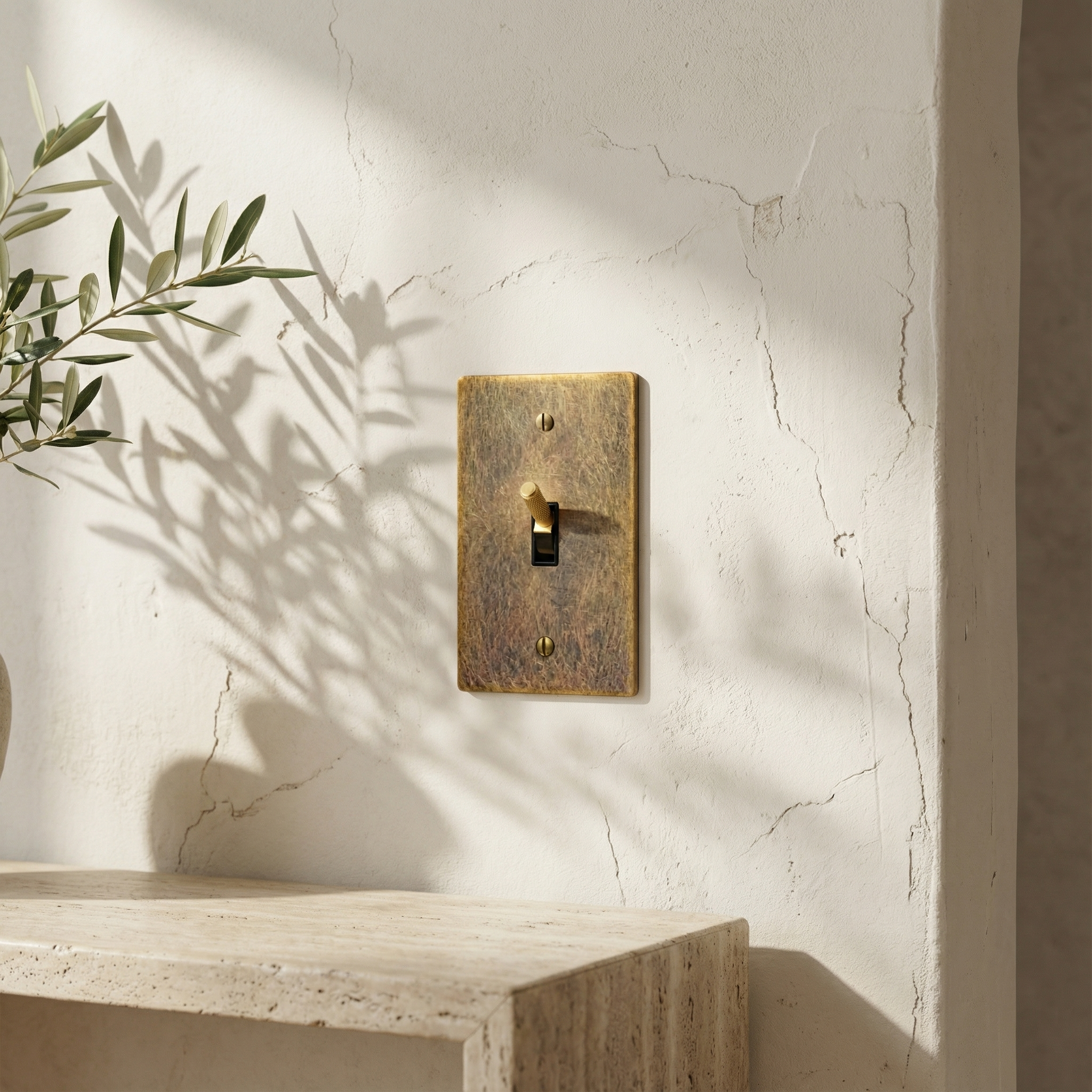 Aged brass 1 gang toggle switch plate on a subtly textured wall, bathed in sunlight with olive shadows, evokes quiet luxury.