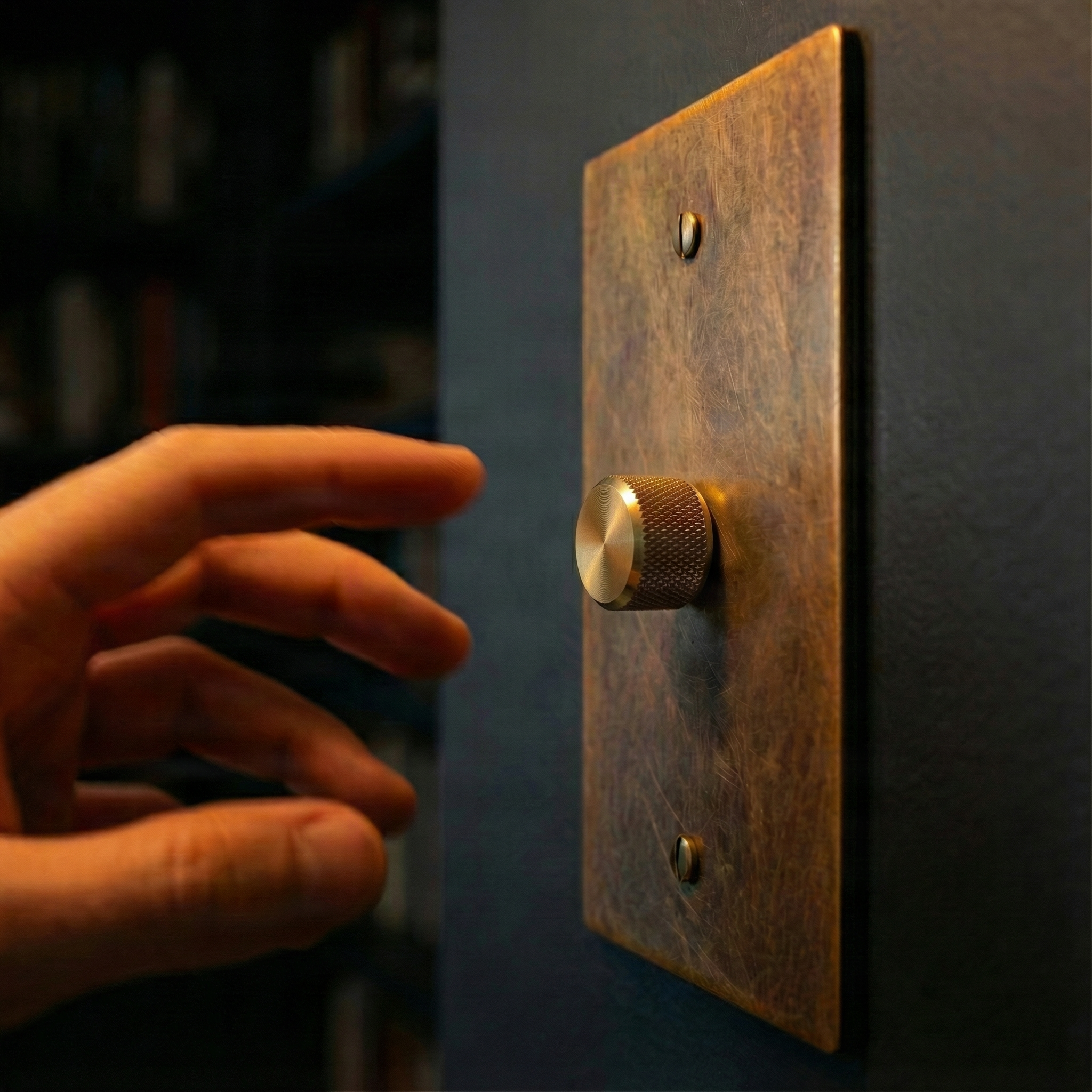 Hand reaching for a Metal Workz aged brass 1 gang dimmer switch plate with knurled knob on a dark wall, evoking timeless elegance.