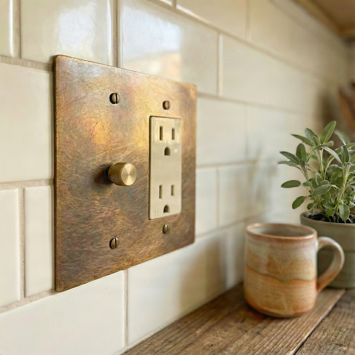 Heirloom aged brass 2 gang dimmer and duplex outlet switch plate accents a kitchen with white tiles and wood.