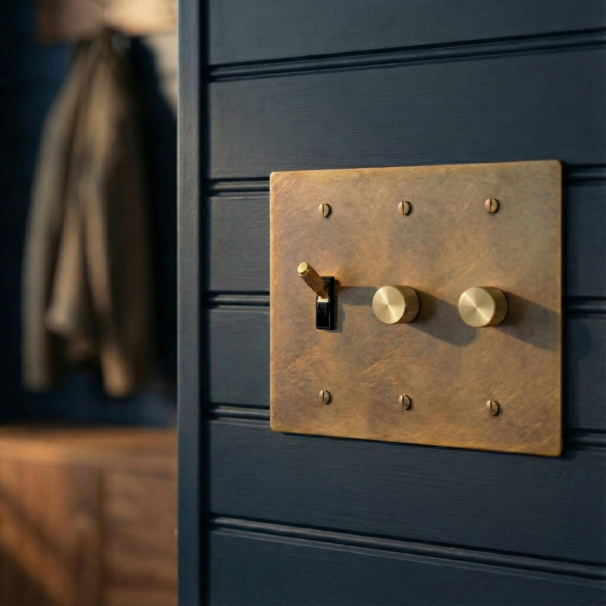 Aged brass 3 gang dimmer and toggle switch plate on a navy paneled wall, evoking quiet luxury in a timeless setting.