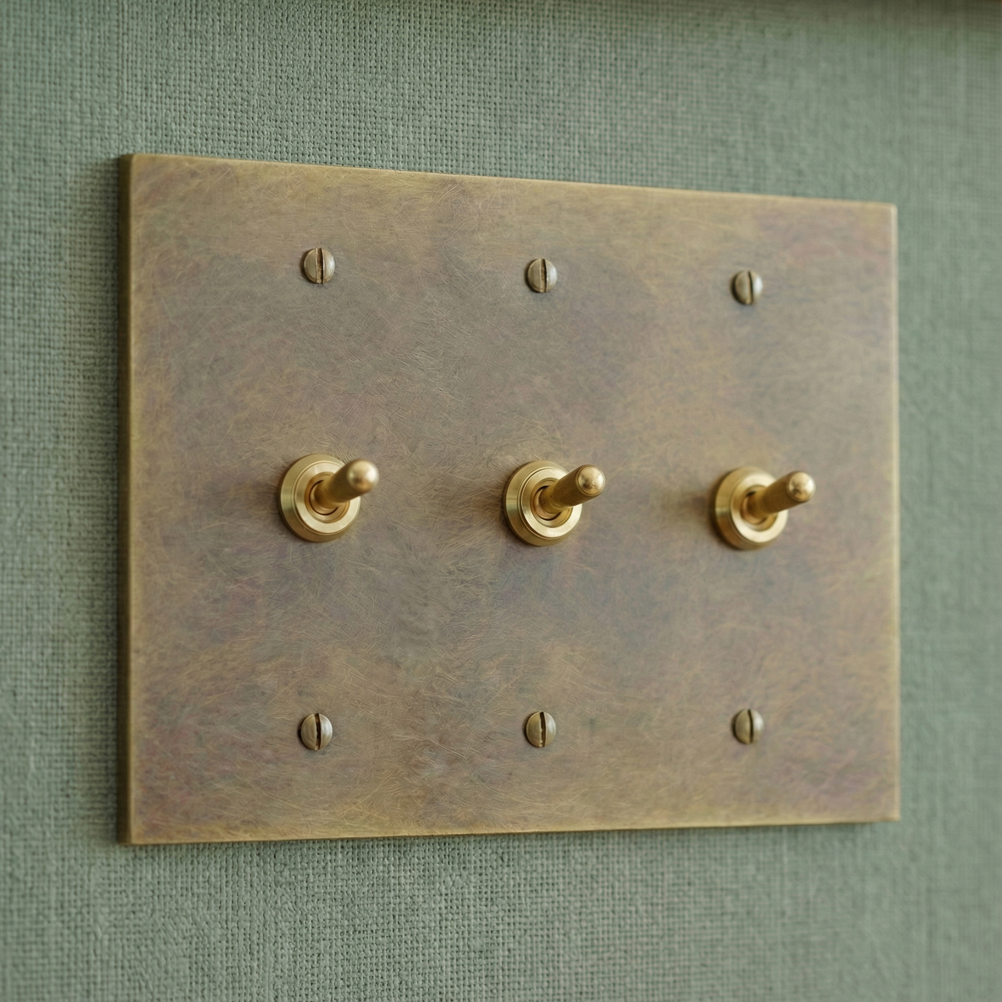aged brass 3 gang vintage toggle switch plate on a muted green textured wall, embodying quiet luxury.