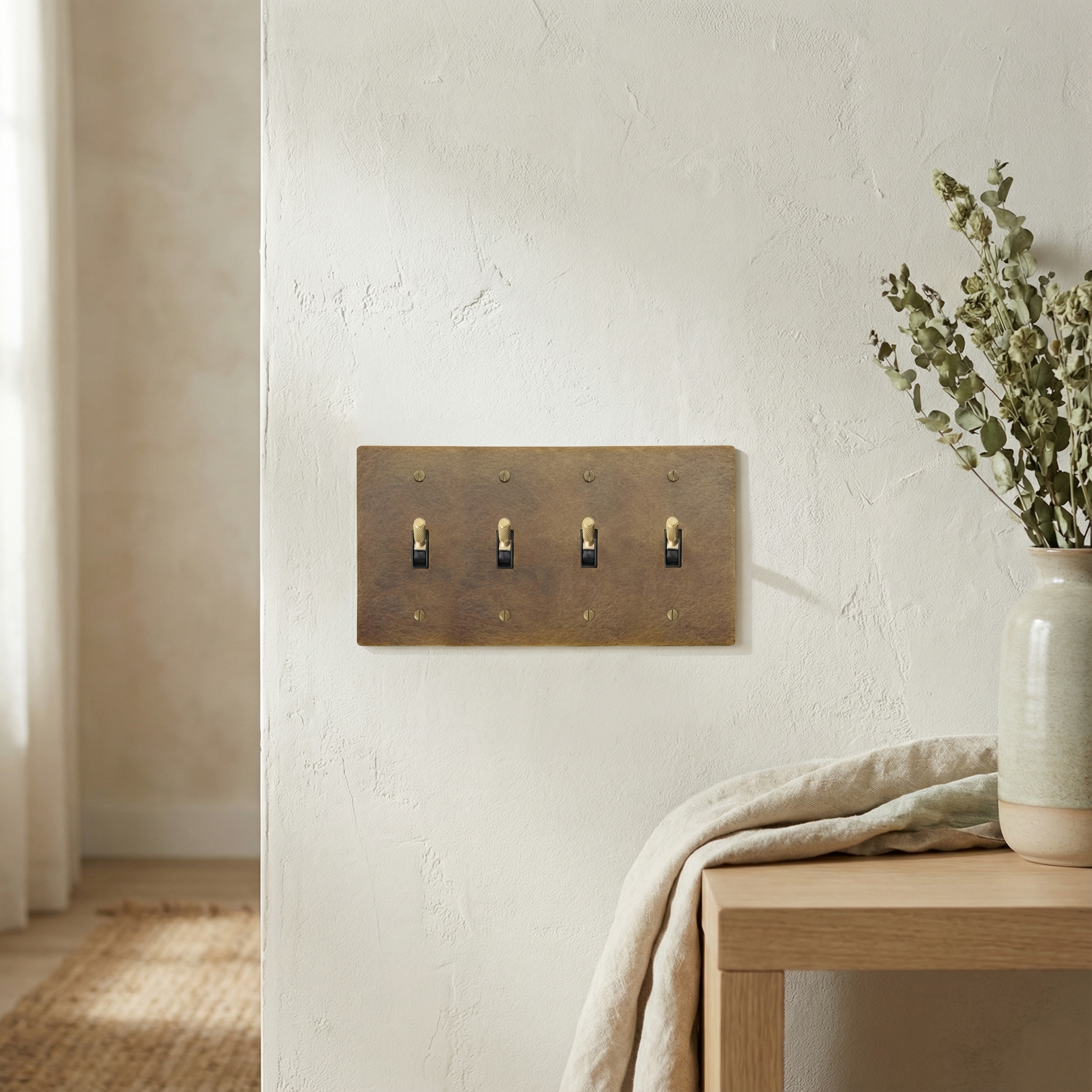 Crafted aged brass 4 gang toggle switch plate on a textured wall, adding timeless elegance to the minimalist setting.
