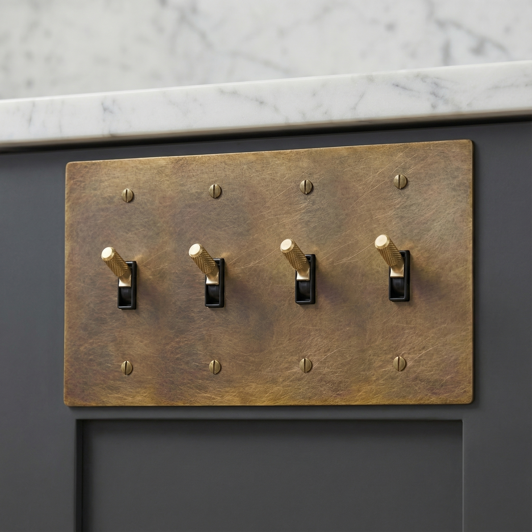 Elegant aged brass 4 gang toggle switch plate, knurled toggles, on gray cabinet below marble.