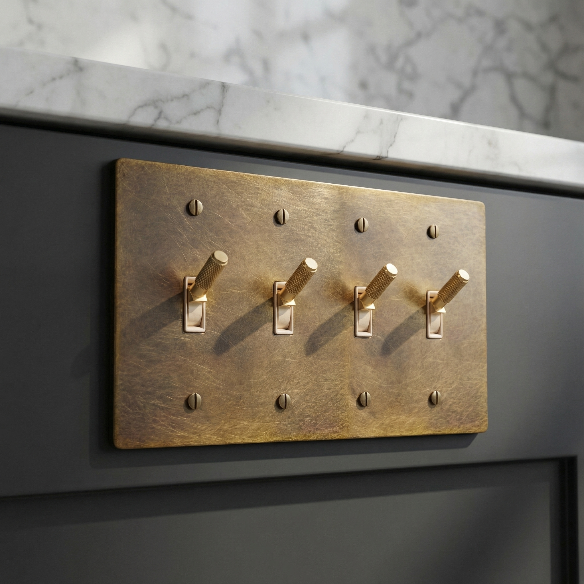 Aged brass 4 gang toggle switch plate on dark cabinetry beneath marble, a statement of quiet luxury.