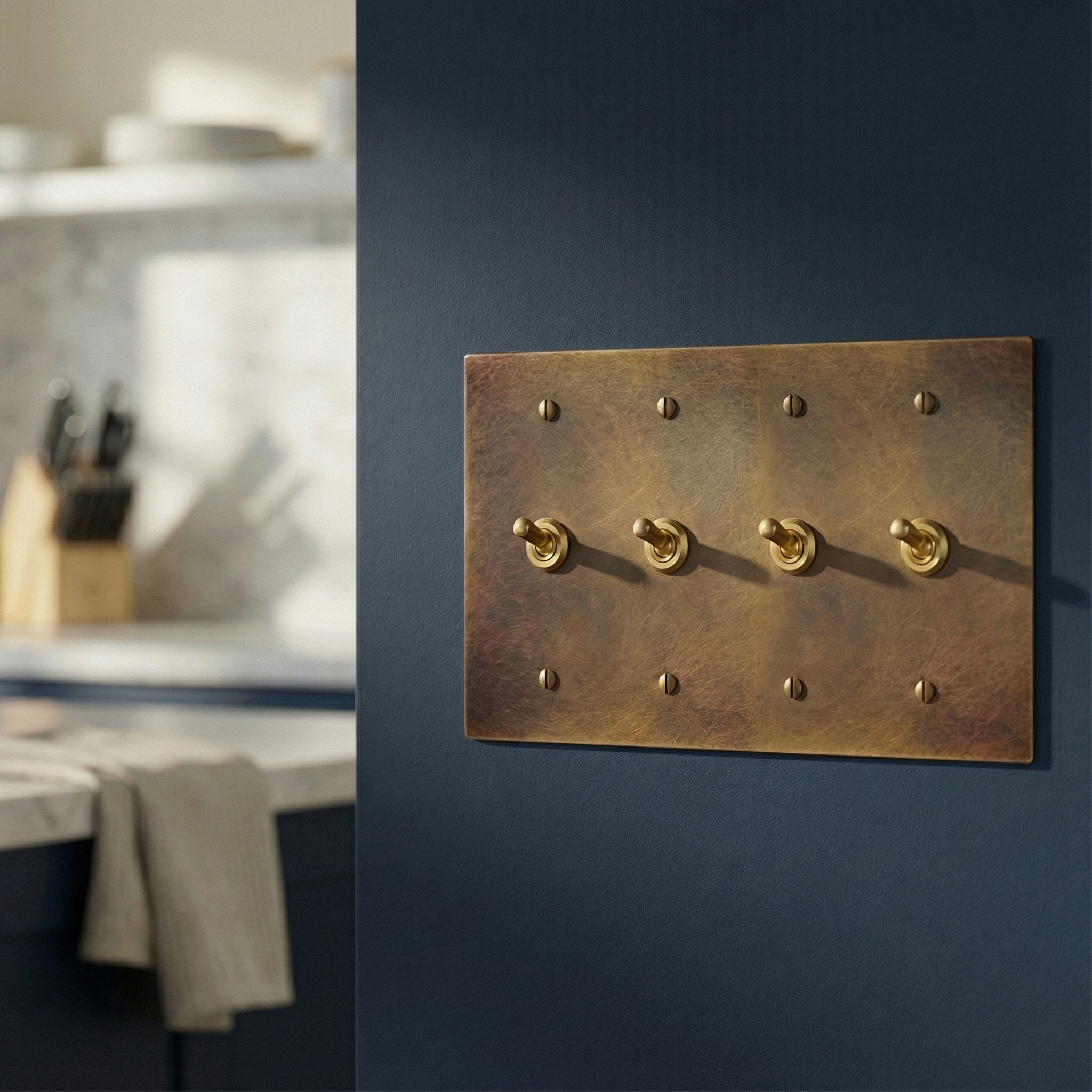 Aged brass 4 gang vintage toggle switch plate on a navy wall in an elegant, blurred kitchen, embodying quiet luxury.
