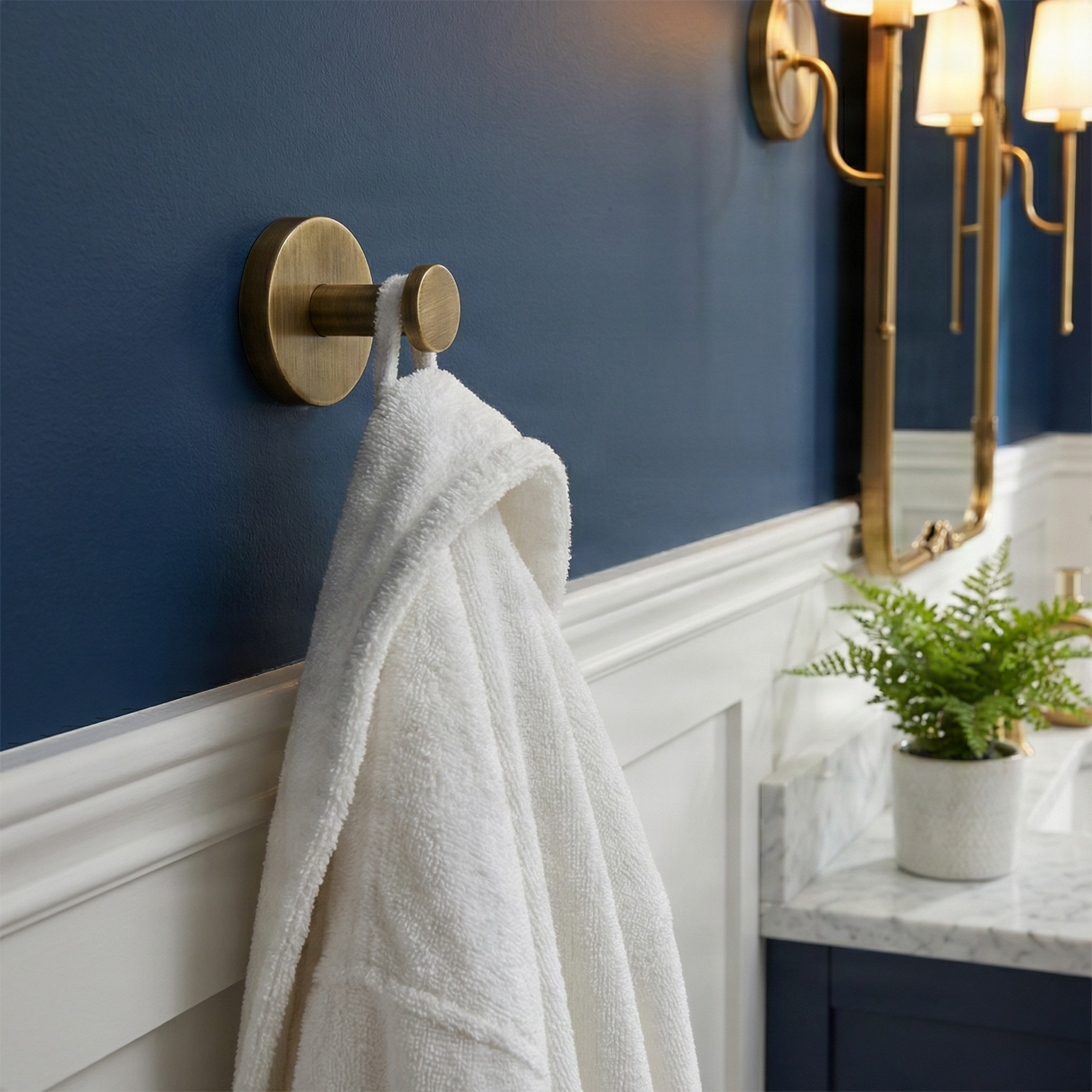 knurled aged brass towel hook on deep blue wall holding a white robe in an elegant bathroom.