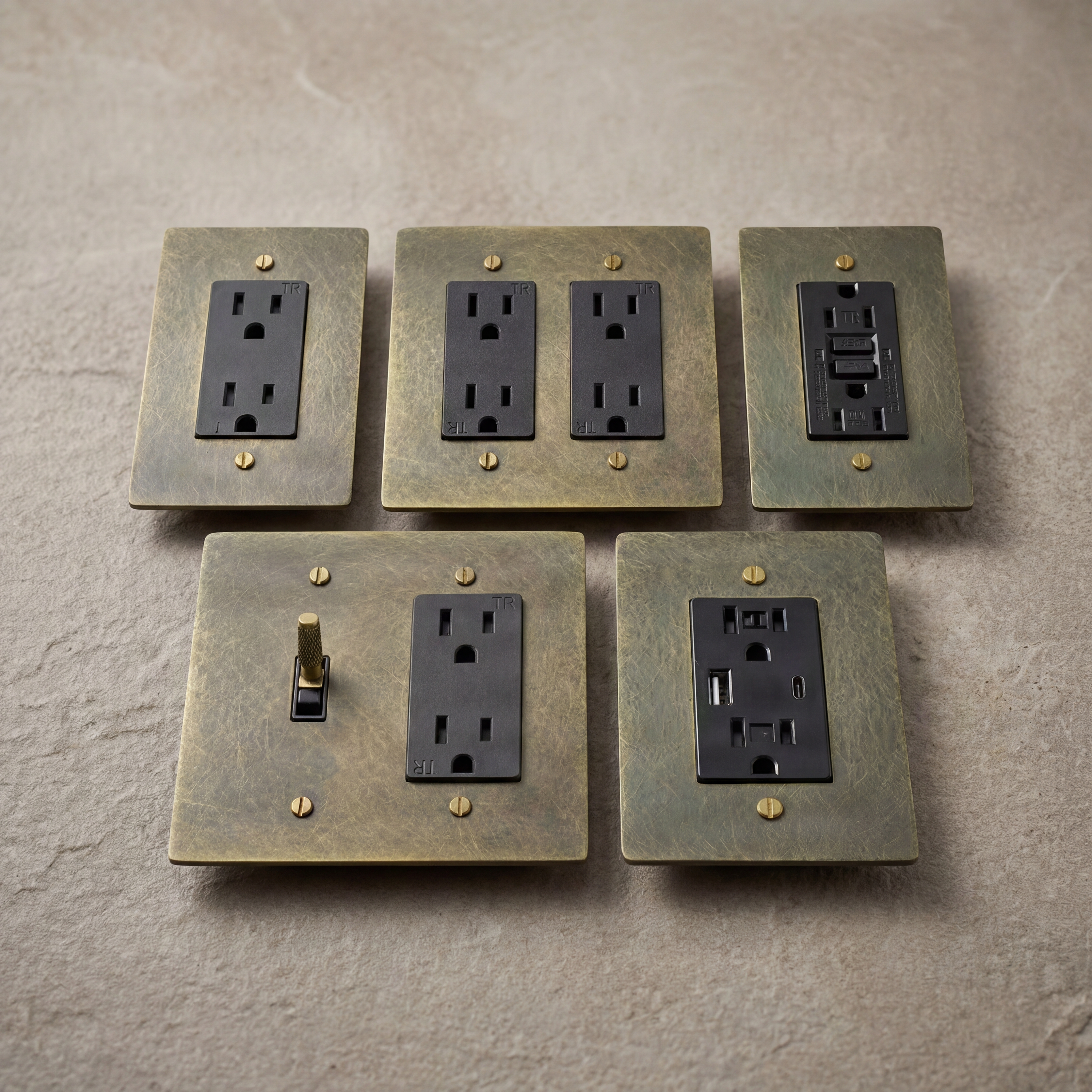 Patinated antique brass outlets, switch, and GFCI on stone.