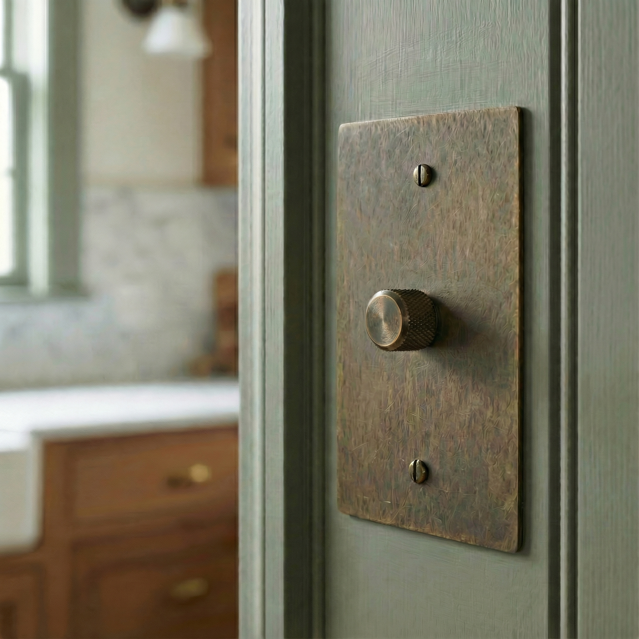 Antique brass 1 gang dimmer switch plate on a sage green wall, exuding timeless craftsmanship in an elegant kitchen.
