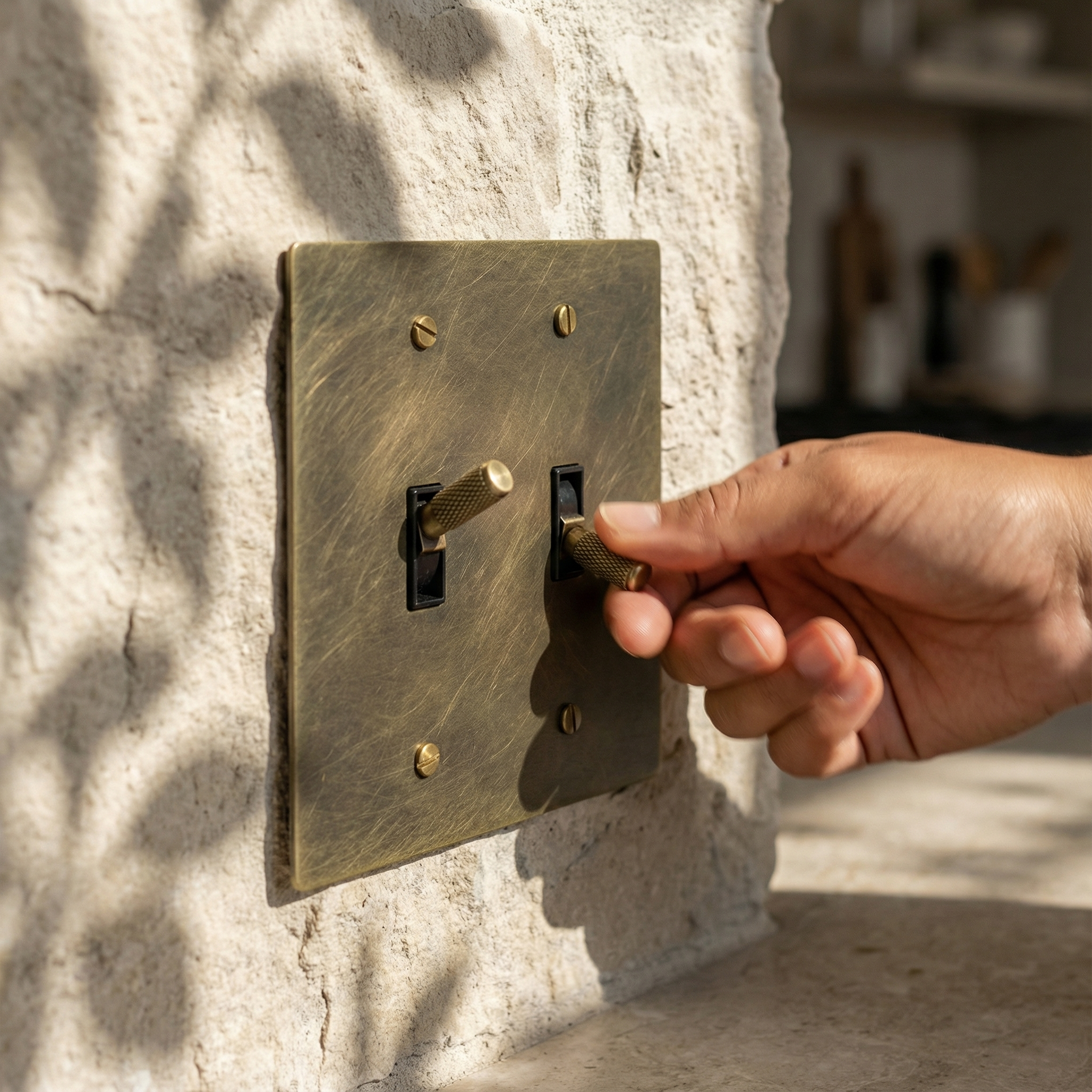 A hand engages an antique brass 2 gang toggle switch plate, accentuating timeless elegance on textured stone.