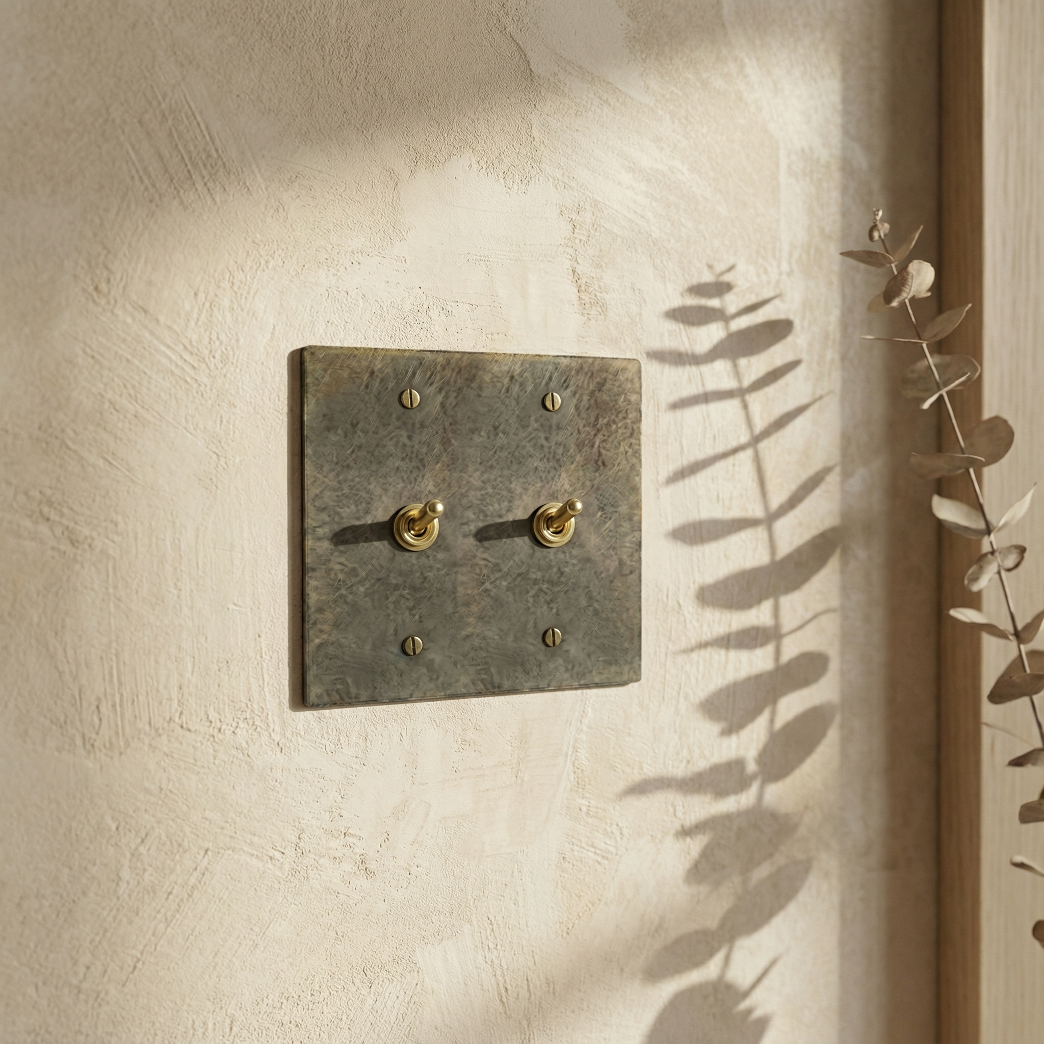 antique brass 2 gang vintage toggle switch plate on a serene, textured wall, bathed in natural light and shadow.