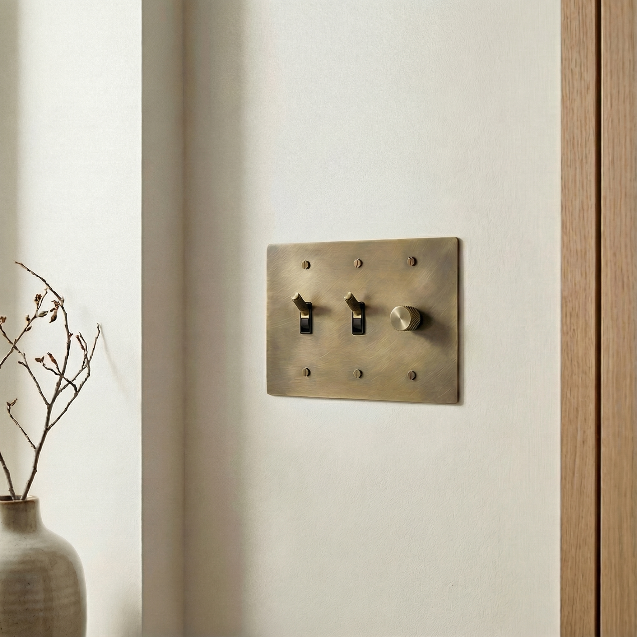 Elegant antique brass 3 gang dimmer and toggle switch plate on a cream wall with a wood door frame.