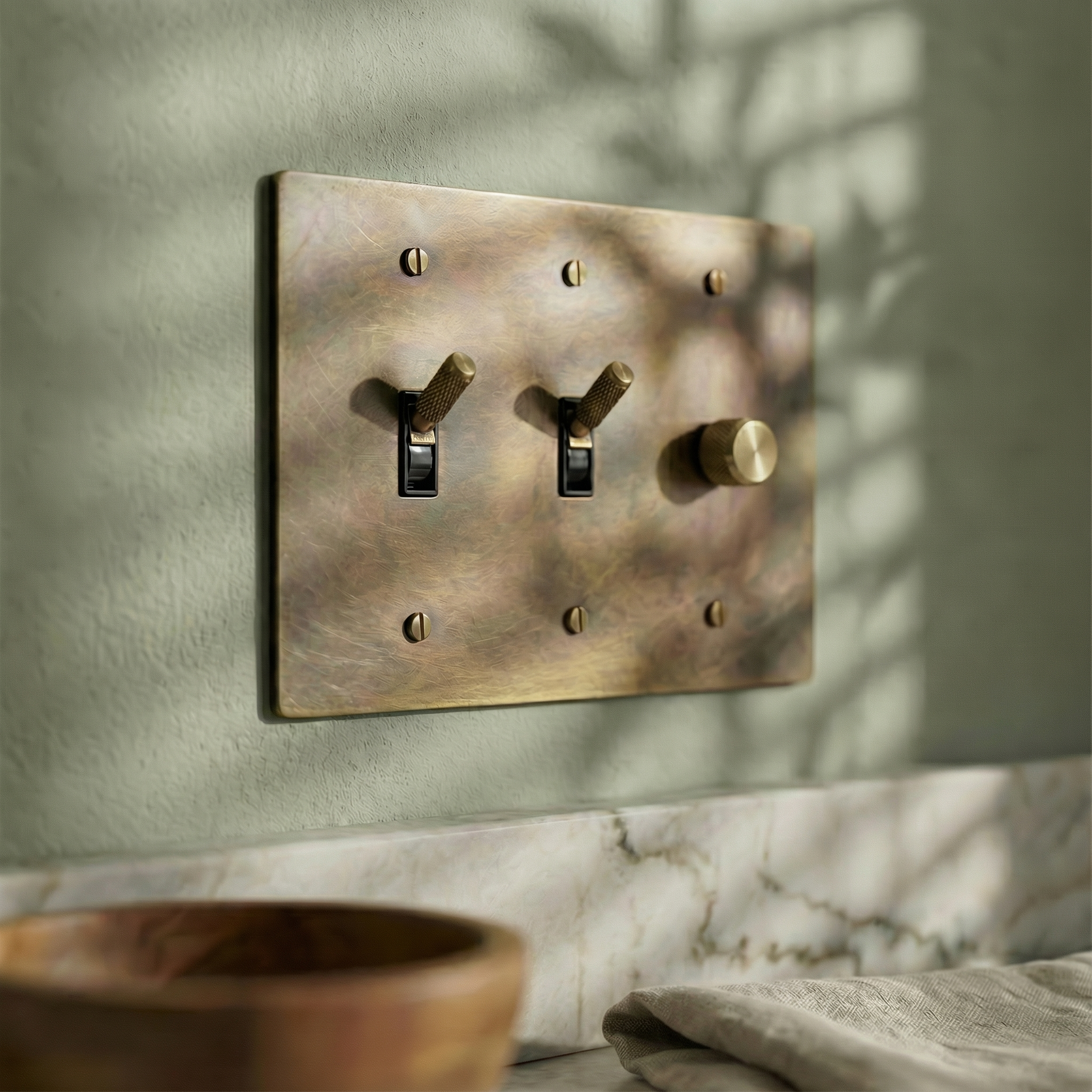 antique brass 3 gang dimmer and toggle switch plate on a serene green wall above marble, evoking quiet luxury.