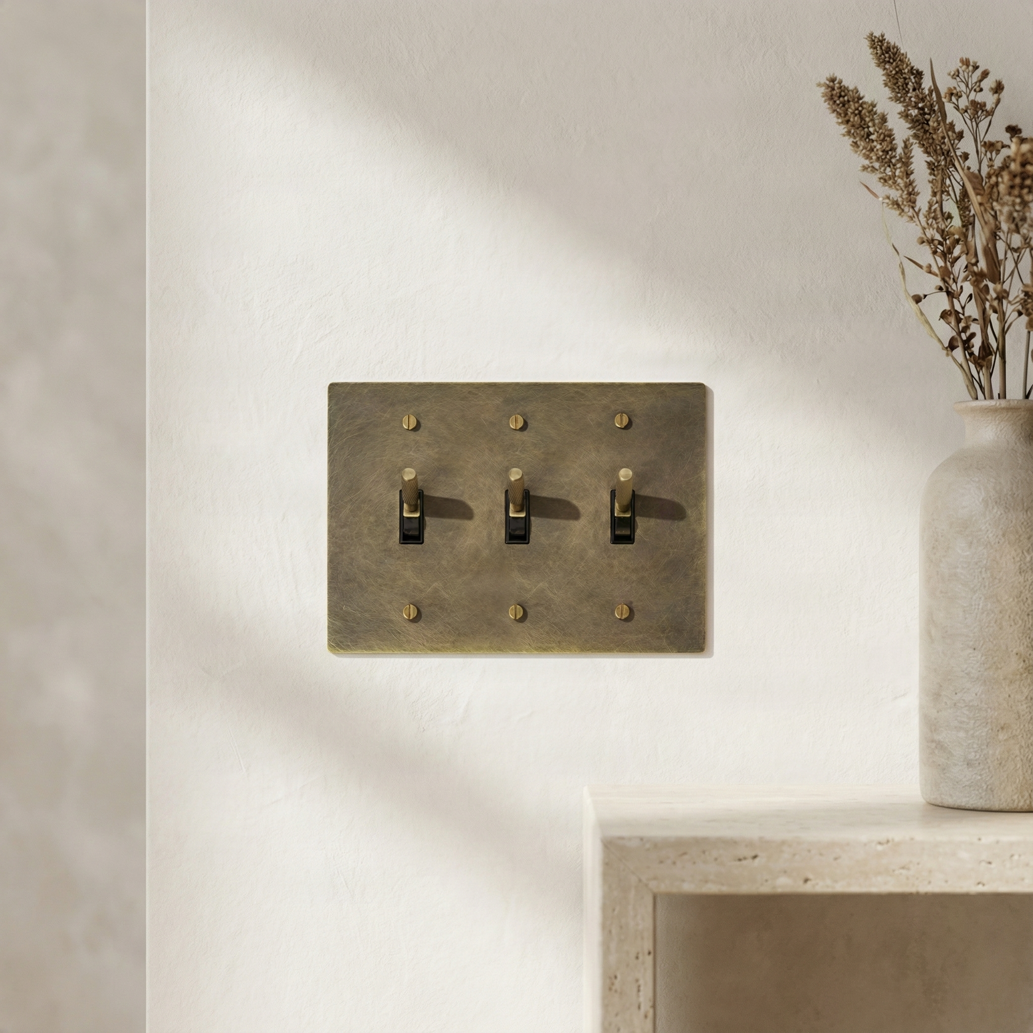 Antique brass 3 gang toggle switch plate on an elegant textured wall, reflecting timeless luxury.