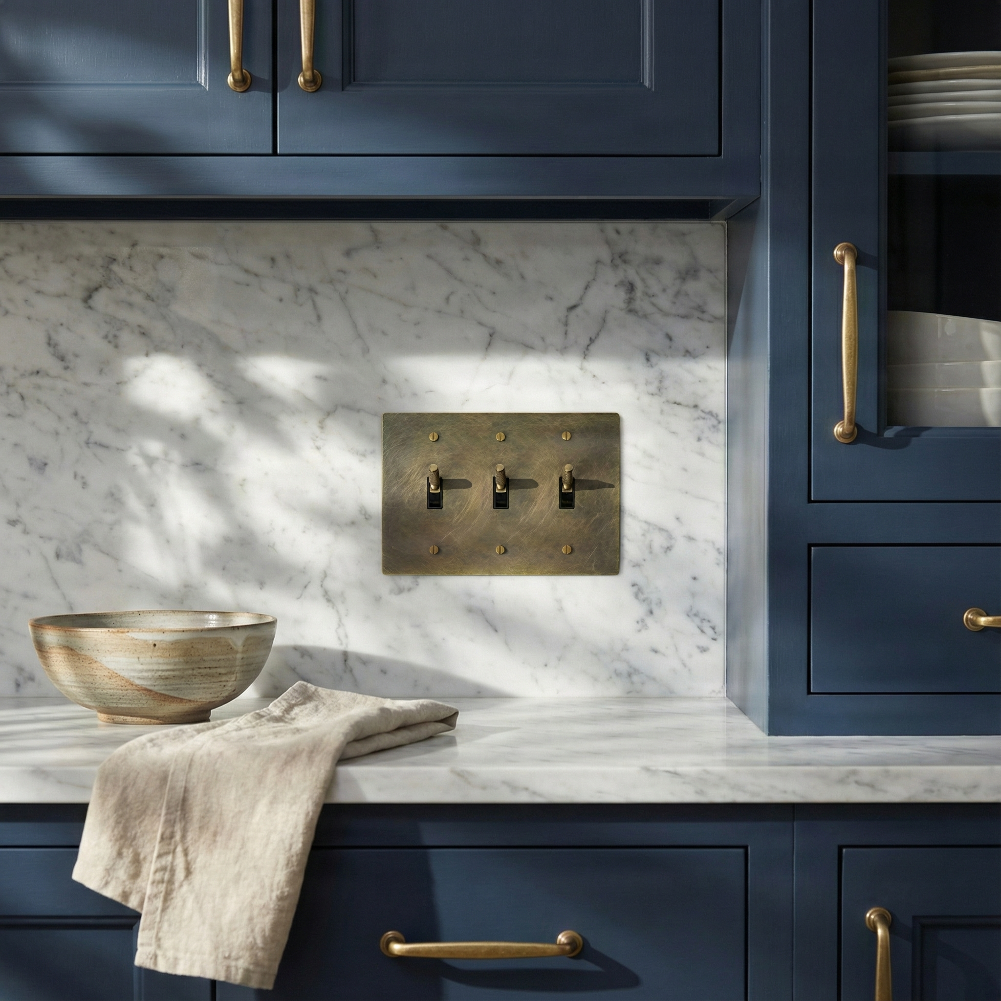 Timeless antique brass 3 gang toggle switch plate on white marble, blending with elegant blue cabinetry.