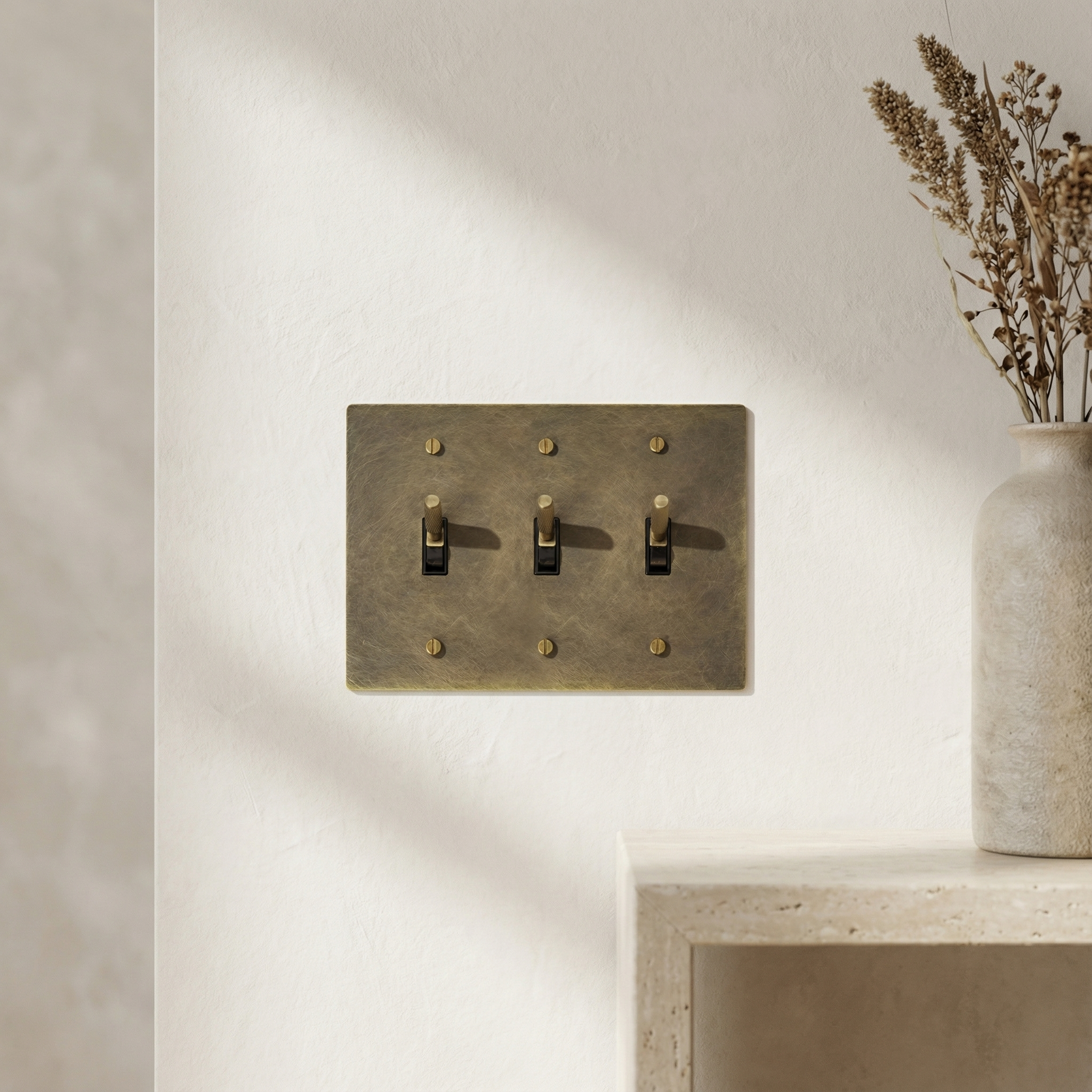 Antique brass 3 gang toggle switch plate on an elegant textured wall, reflecting timeless luxury.