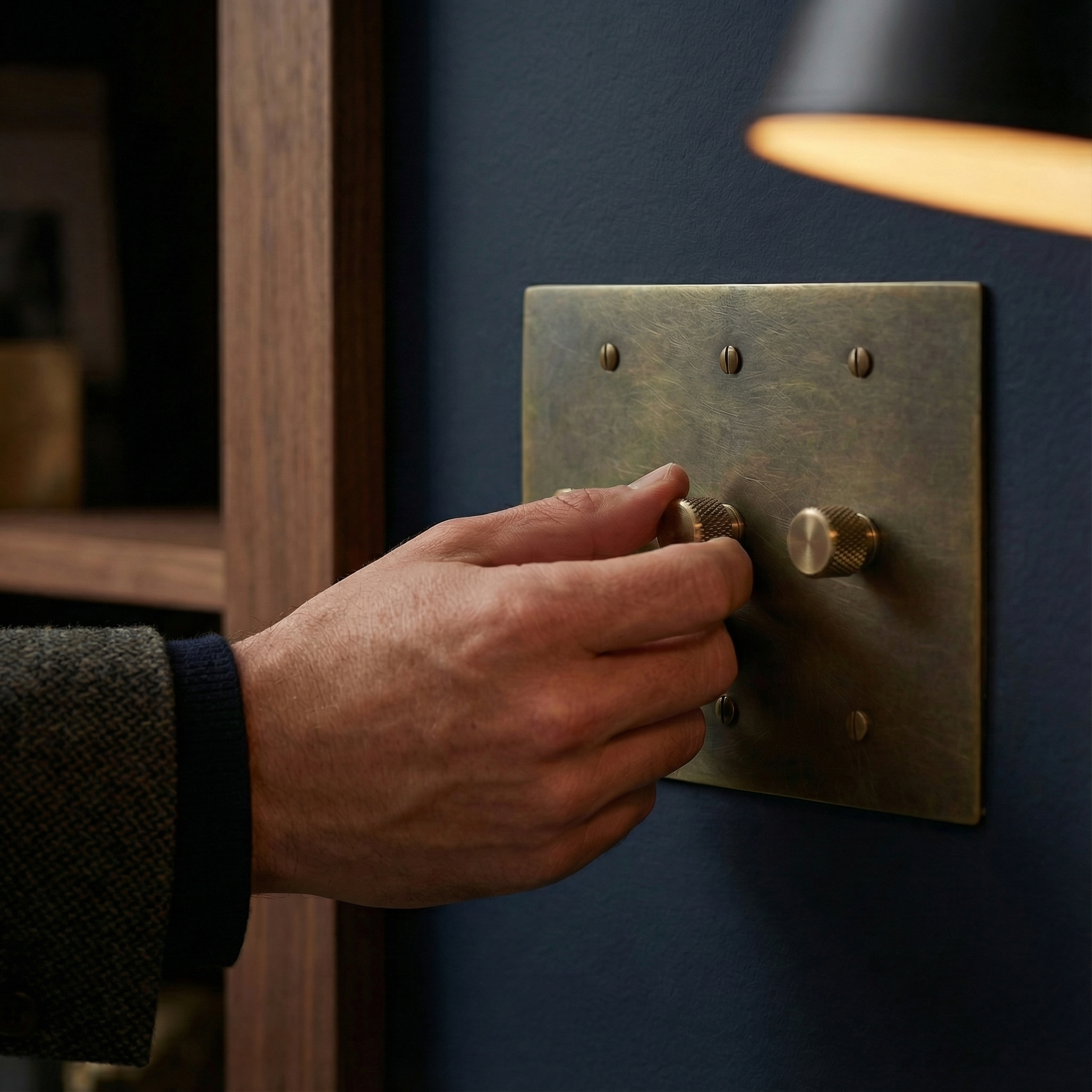 Hand adjusts an antique brass 3 gang dimmer switch plate on a dark wall, evoking timeless elegance.