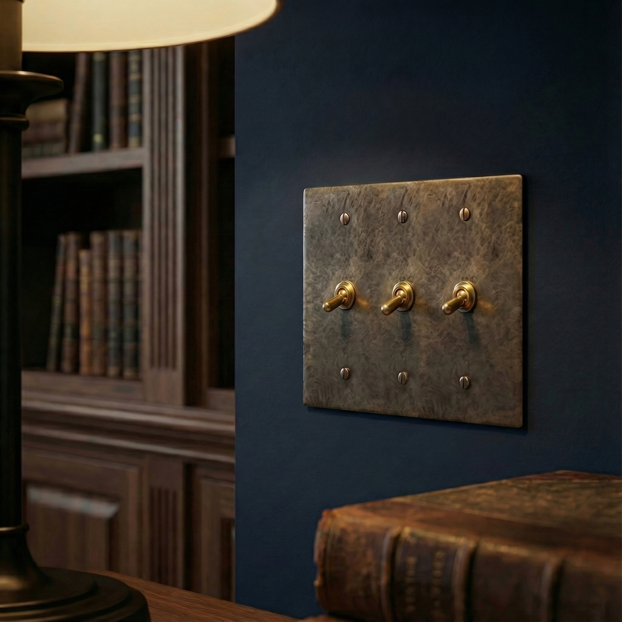 Timeless study featuring a patinated antique brass 3 gang vintage toggle switch plate on a dark wall amidst classic literature.