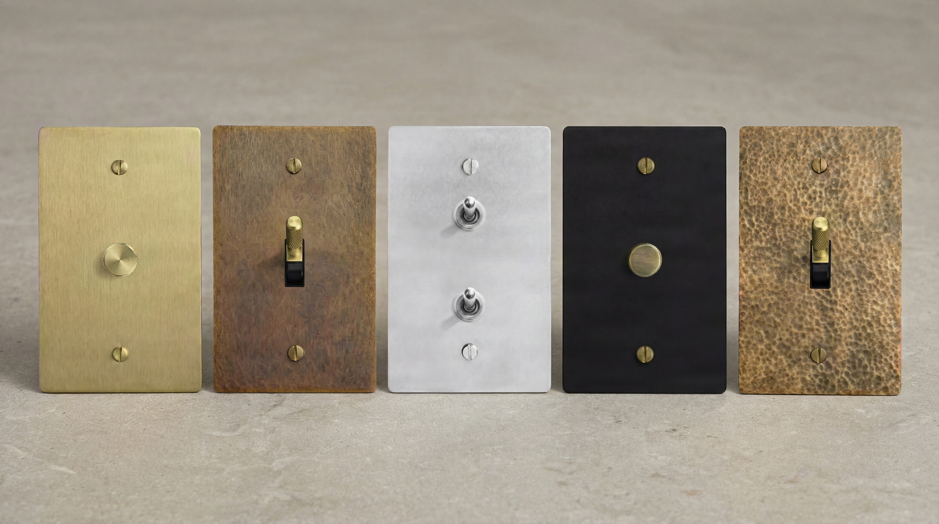 Five heirloom-quality Light Switches: brass, nickel, and matte black with toggles and a dimmer, on a textured background.