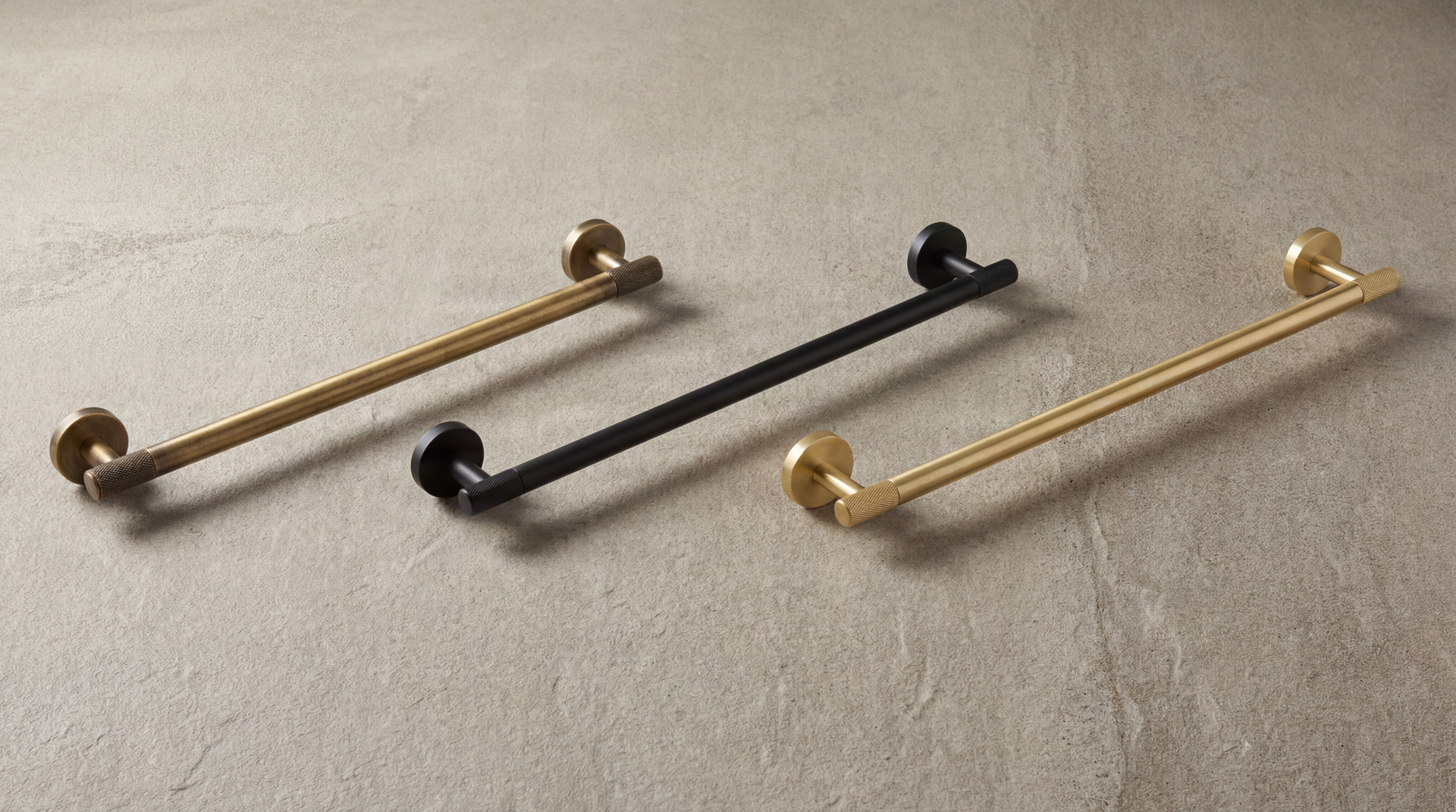 Metal Workz Long Towel Rods: Aged Brass, Matte Black, Satin Brass with knurled details, on a refined concrete surface.
