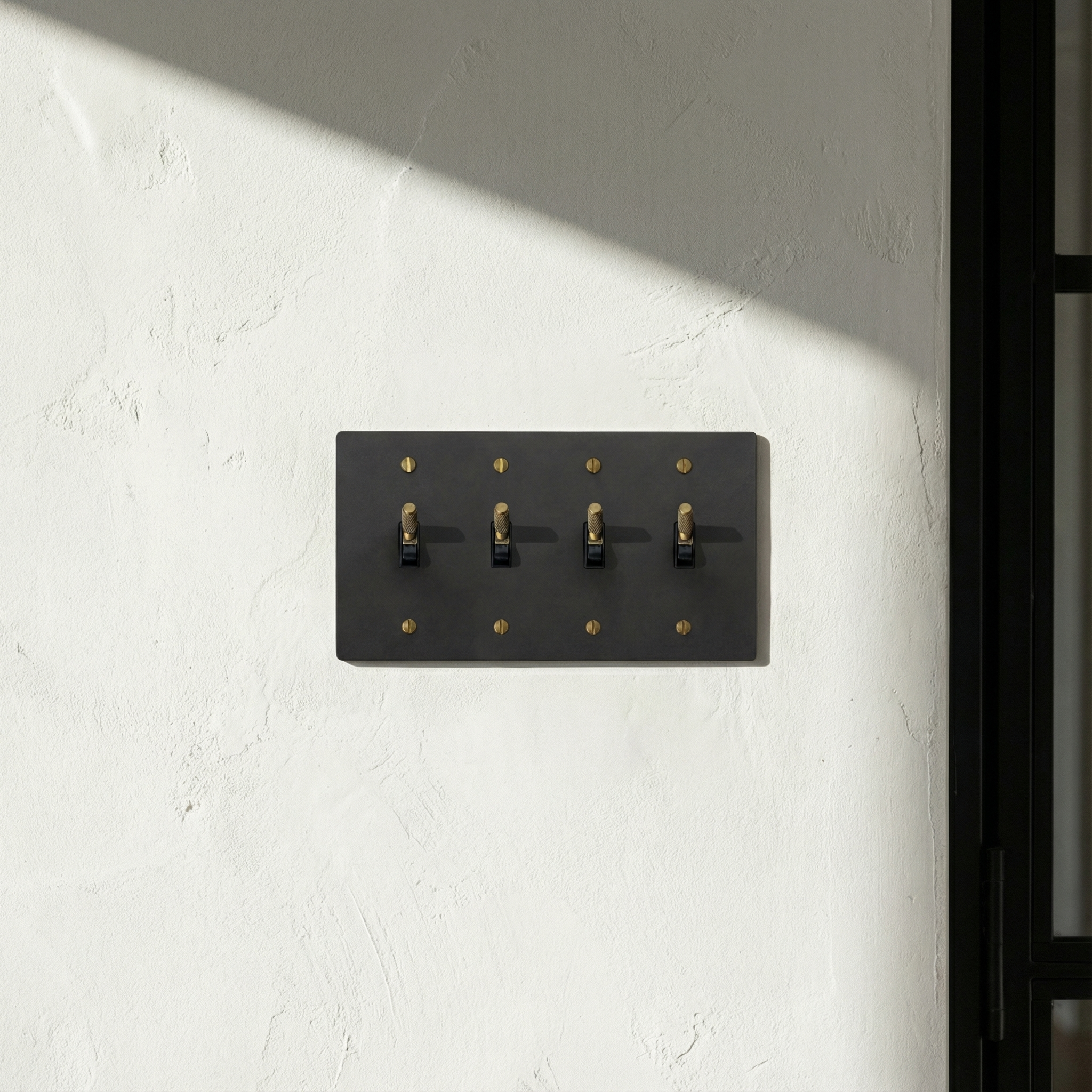 Quiet luxury: matte black (antique brass accents) 4 gang toggle switch plate on a textured wall, with natural light and shadow.