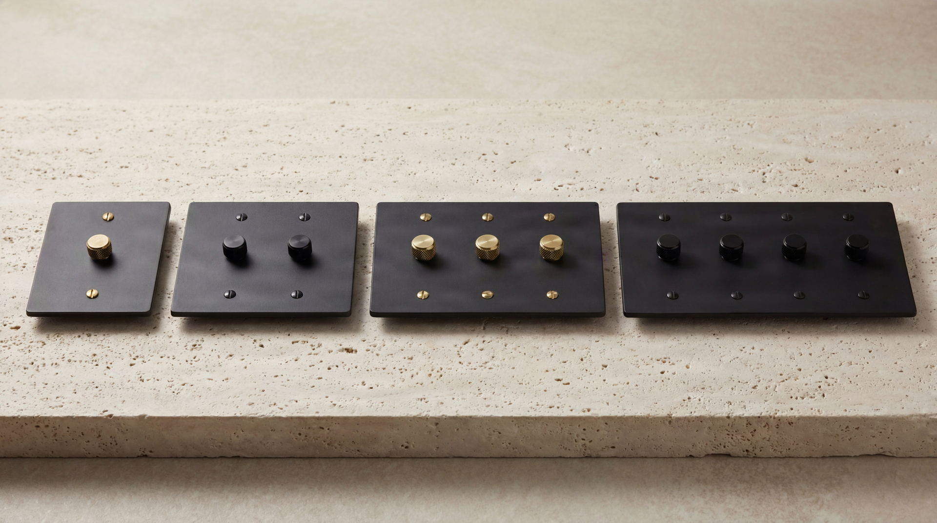 Four elegant Matte Black Dimmer Switches, with varied brass and black knurled knobs, resting on travertine.