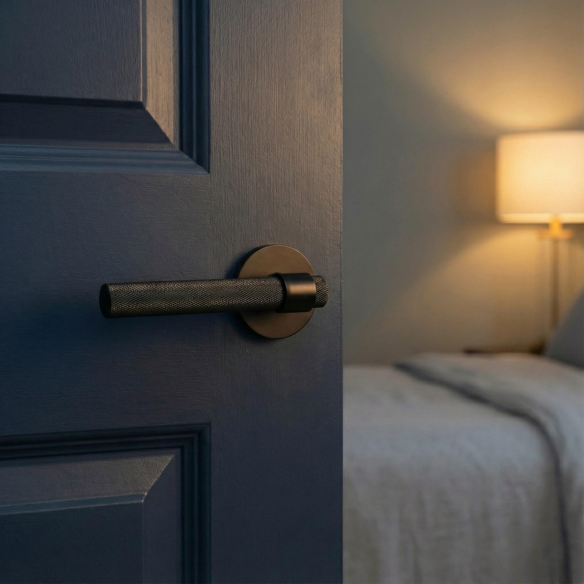 Deep blue door with knurled matte black lever handle opens to an elegant, softly lit bedroom.