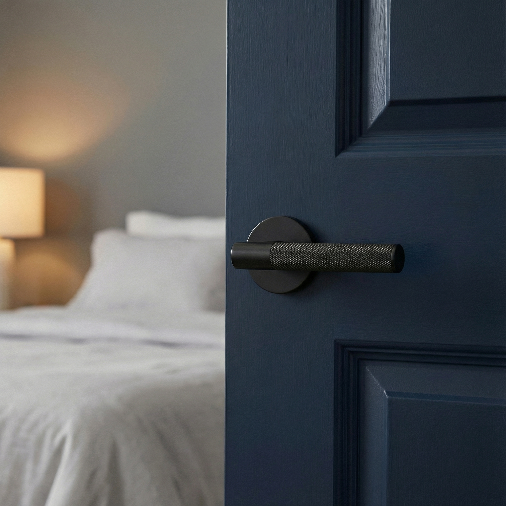 Elegant knurled matte black lever handle on a deep blue door, opening to a tranquil bedroom.