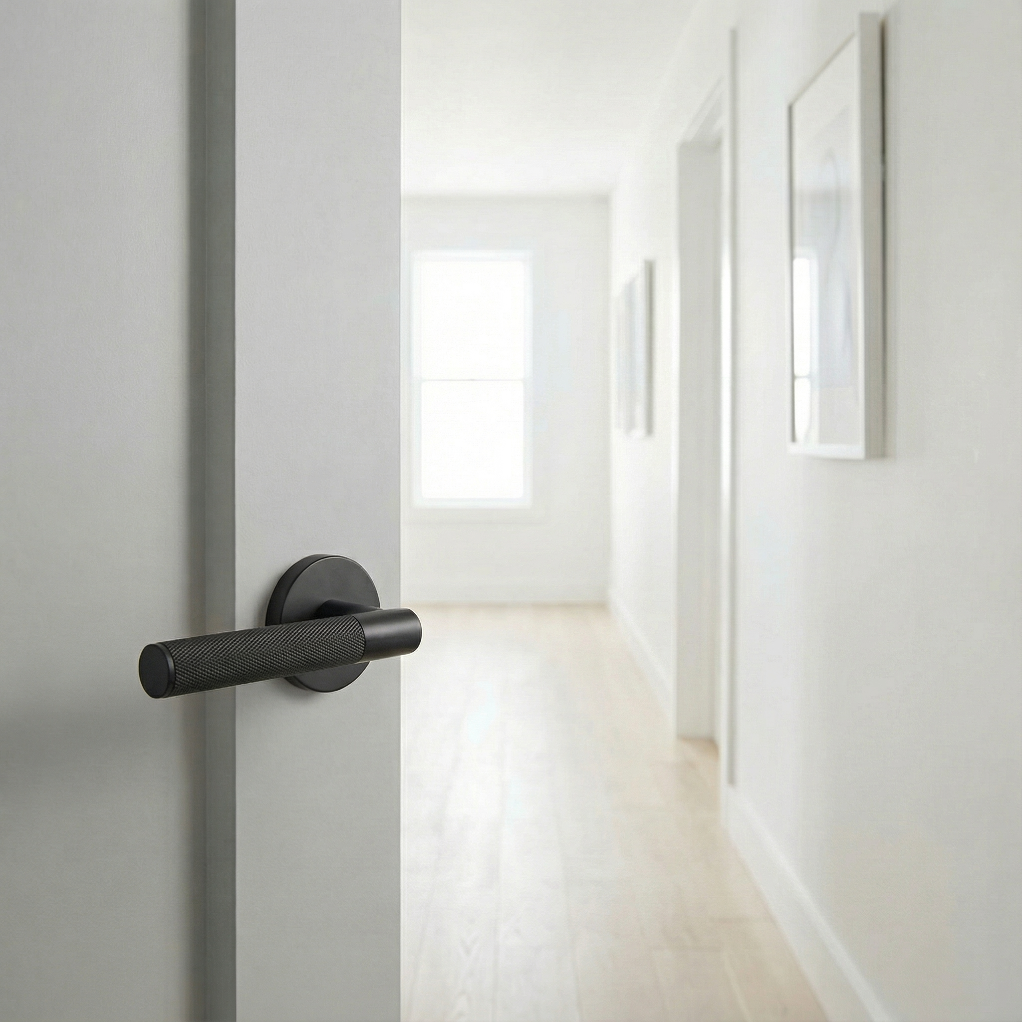 Elegant modern matte black lever handle on a door opening to a bright, timeless hallway with light wood floors.