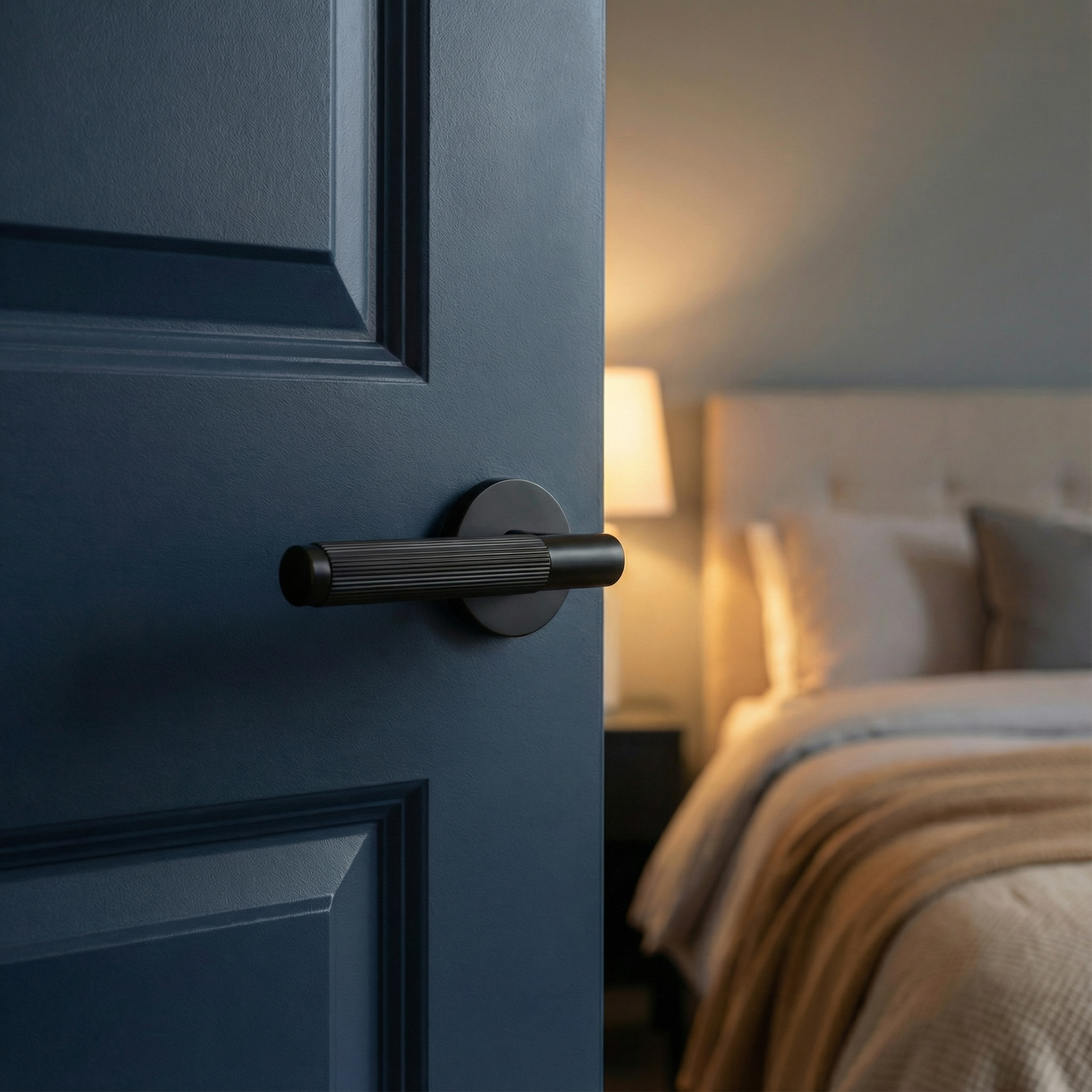 A knurled matte black lever handle on a dark blue door reveals a soft, inviting bedroom.