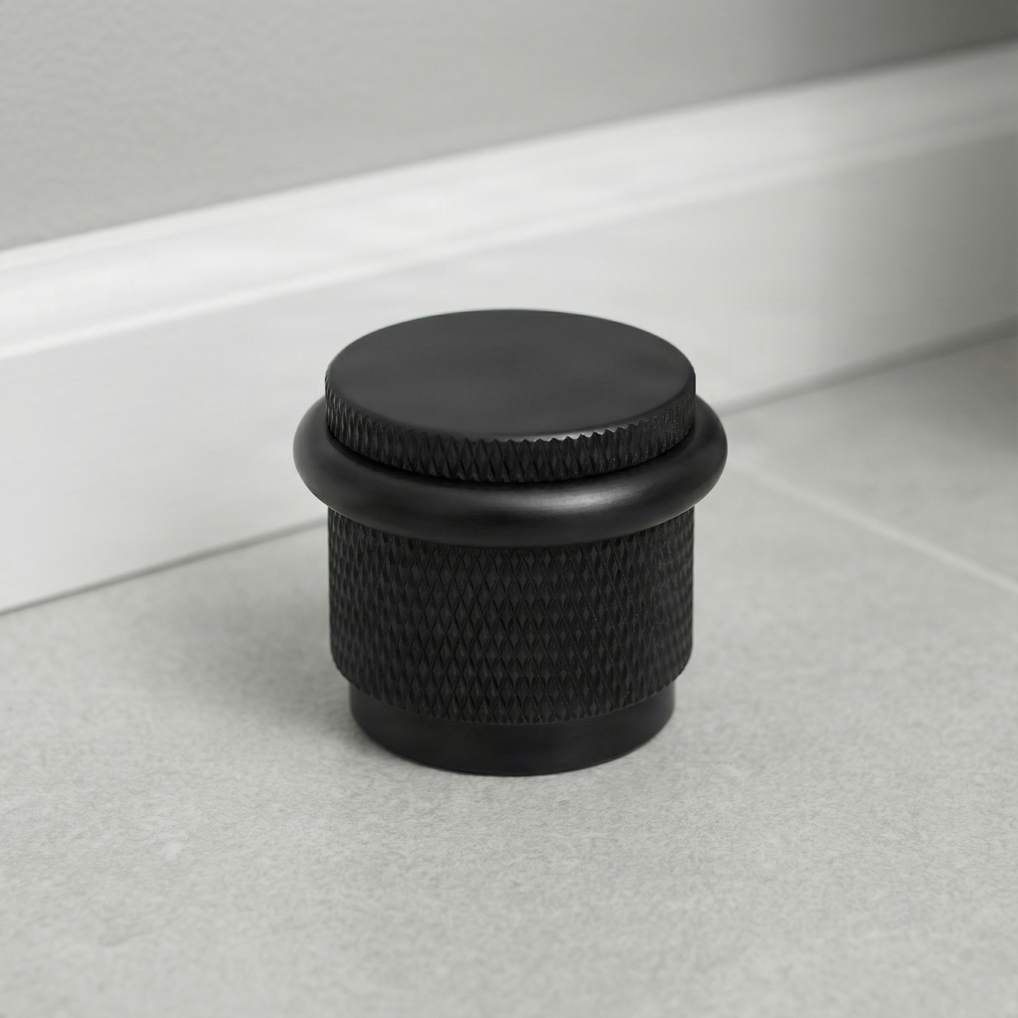 Knurled matte black floor mount door stop on a light tiled floor, conveying timeless elegance.