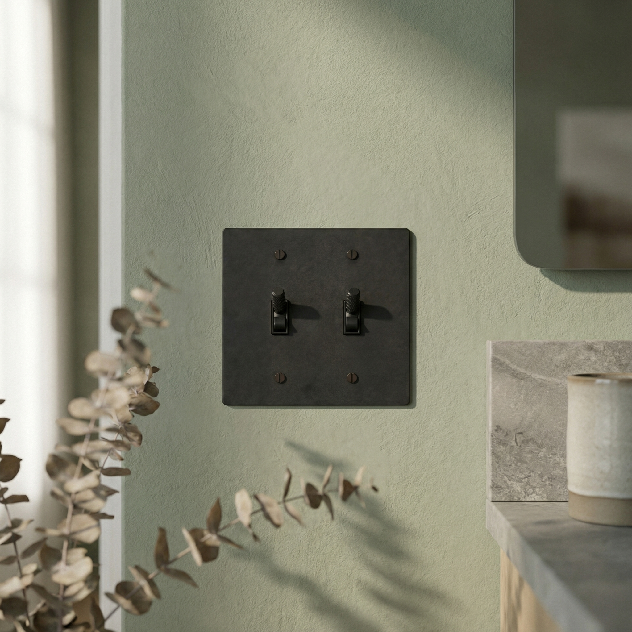 A knurled matte black (matte black accents) 2 gang toggle switch plate on a textured green wall, exuding quiet luxury.
