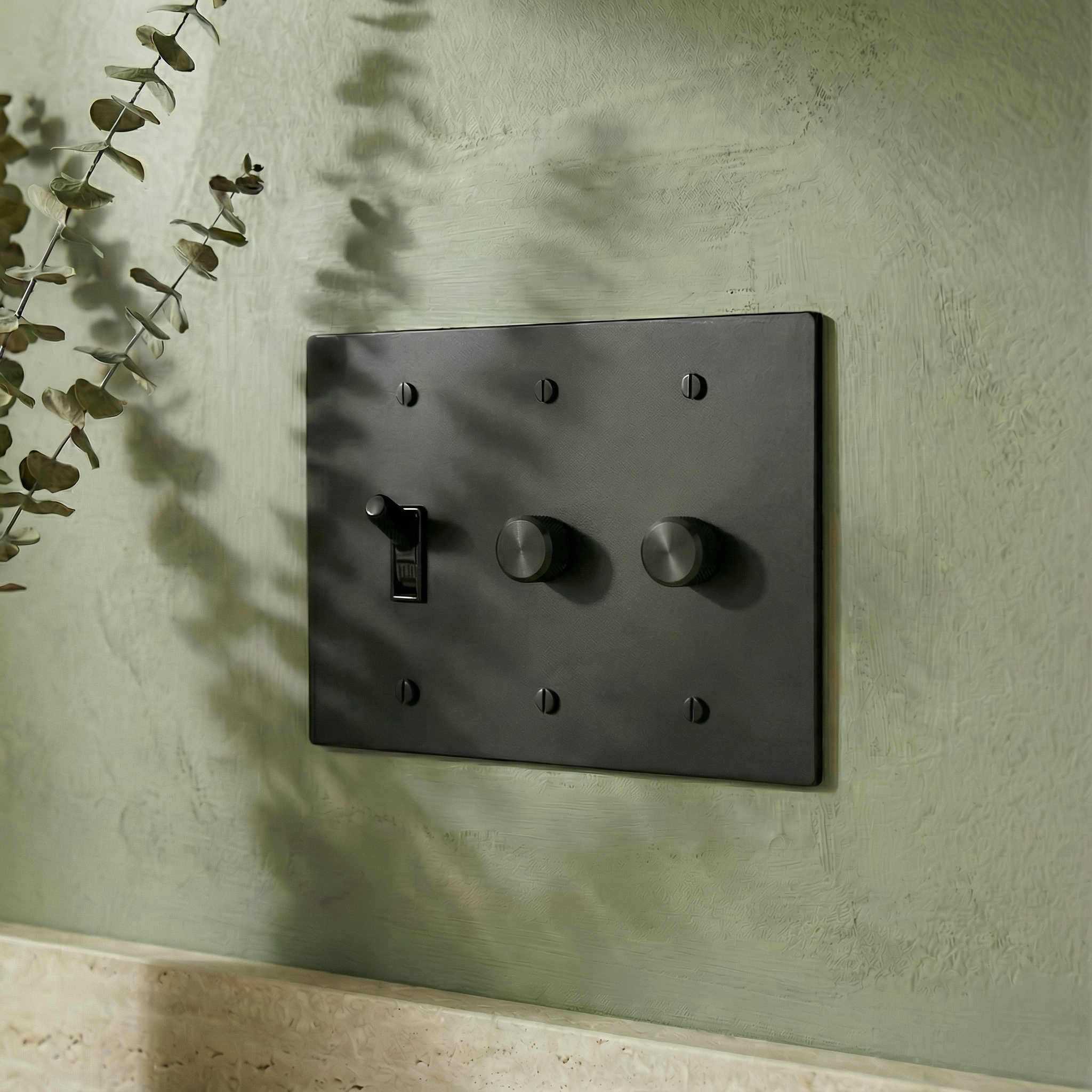 matte black (matte black accents) 3 gang dimmer and toggle switch plate on a textured sage wall with elegant eucalyptus shadows.