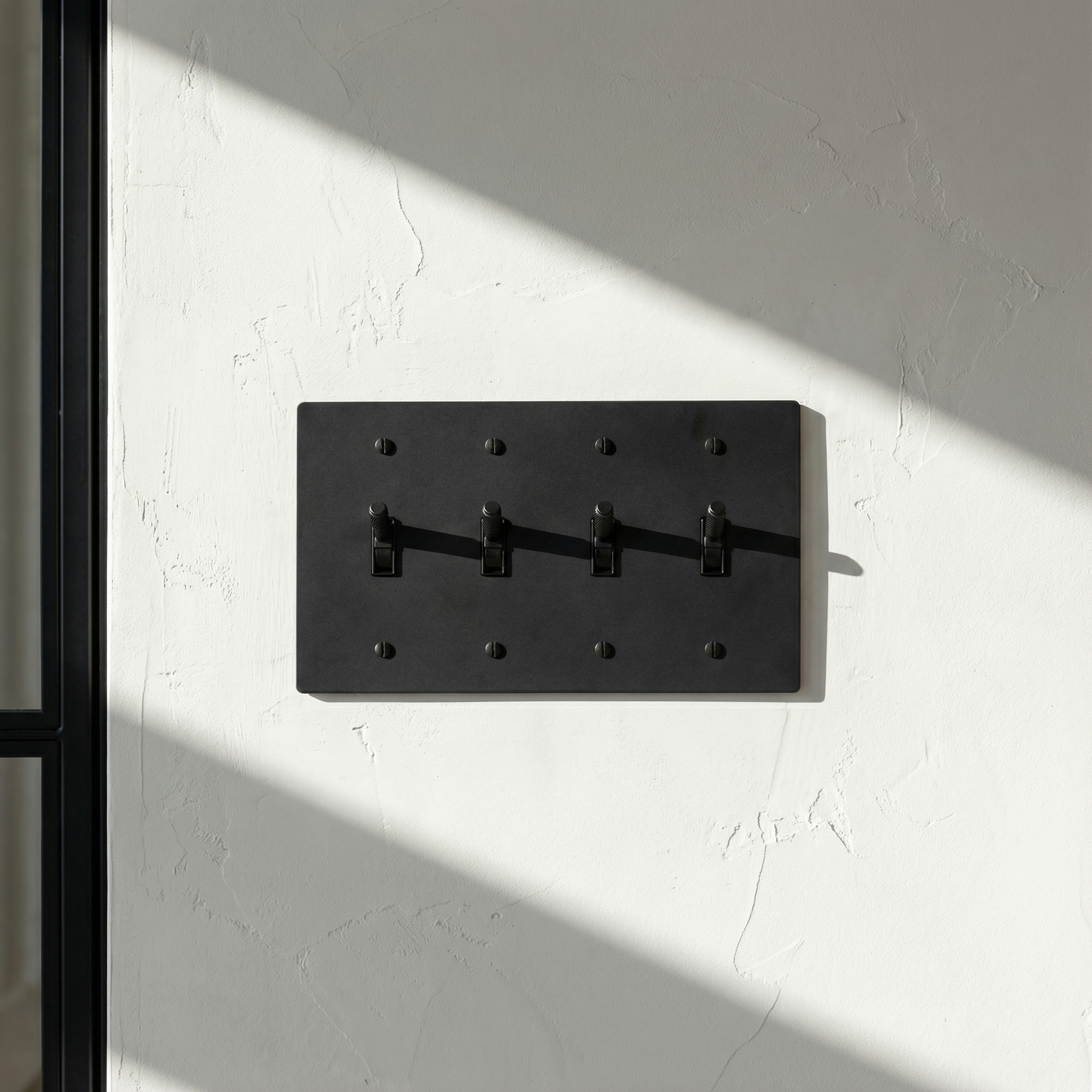 Elegant matte black (matte black accents) 4 gang toggle switch plate on a textured wall, bathed in natural light, evoking timeless luxury.