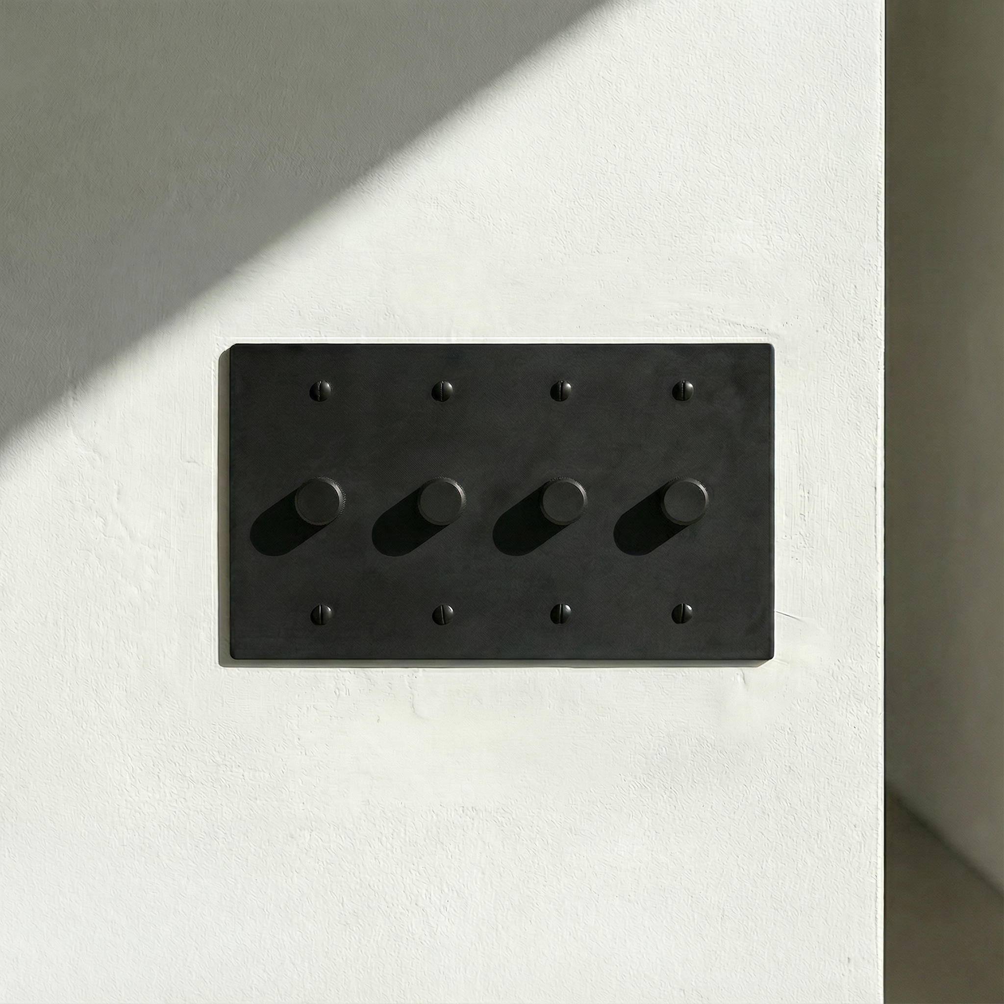 matte black (matte black accents) 4 gang dimmer switch plate on a sunlit, textured white wall. Timeless elegance.