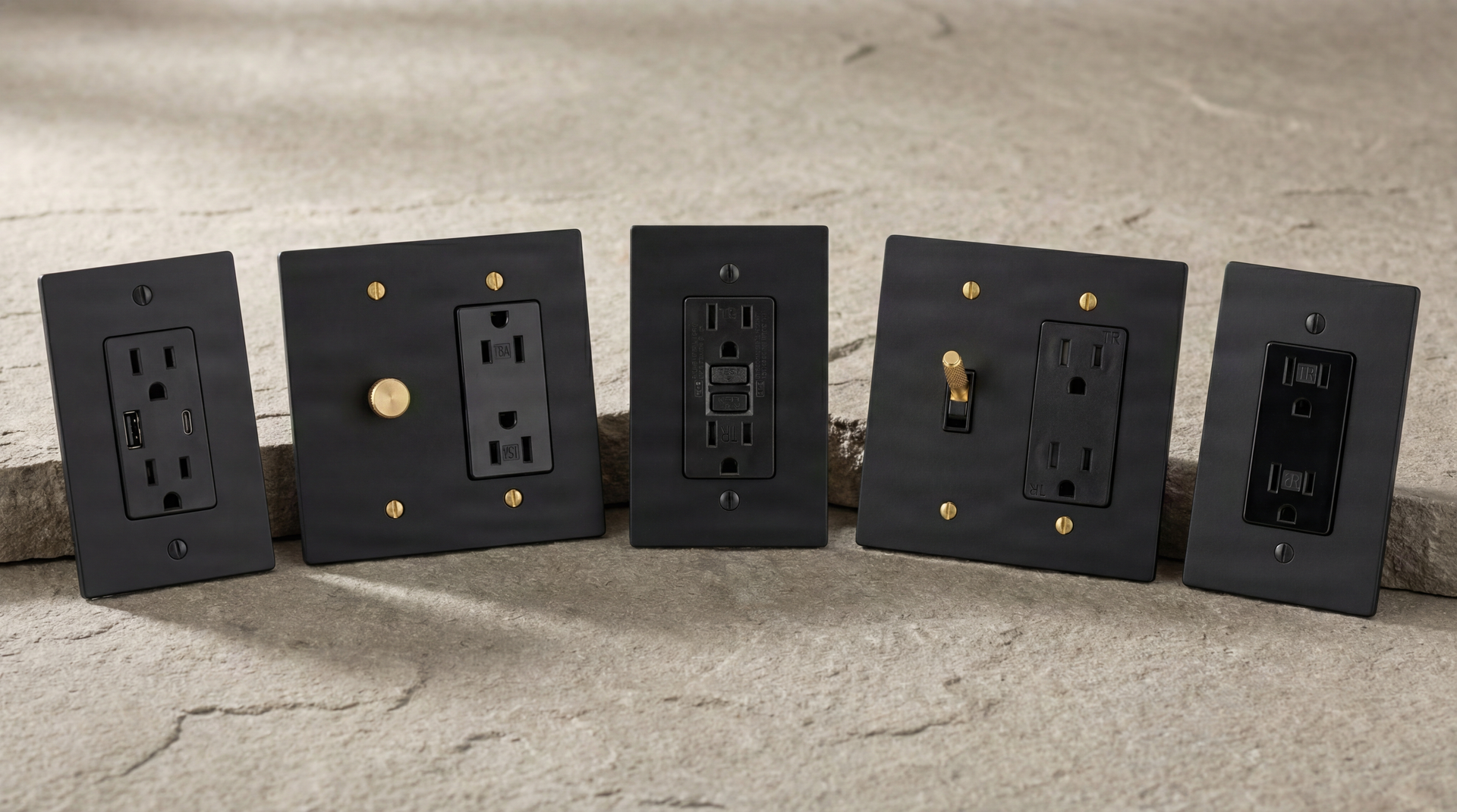 Five finely crafted Matte Black Outlets with brass accents line a stone surface, signaling permanence and quiet luxury.