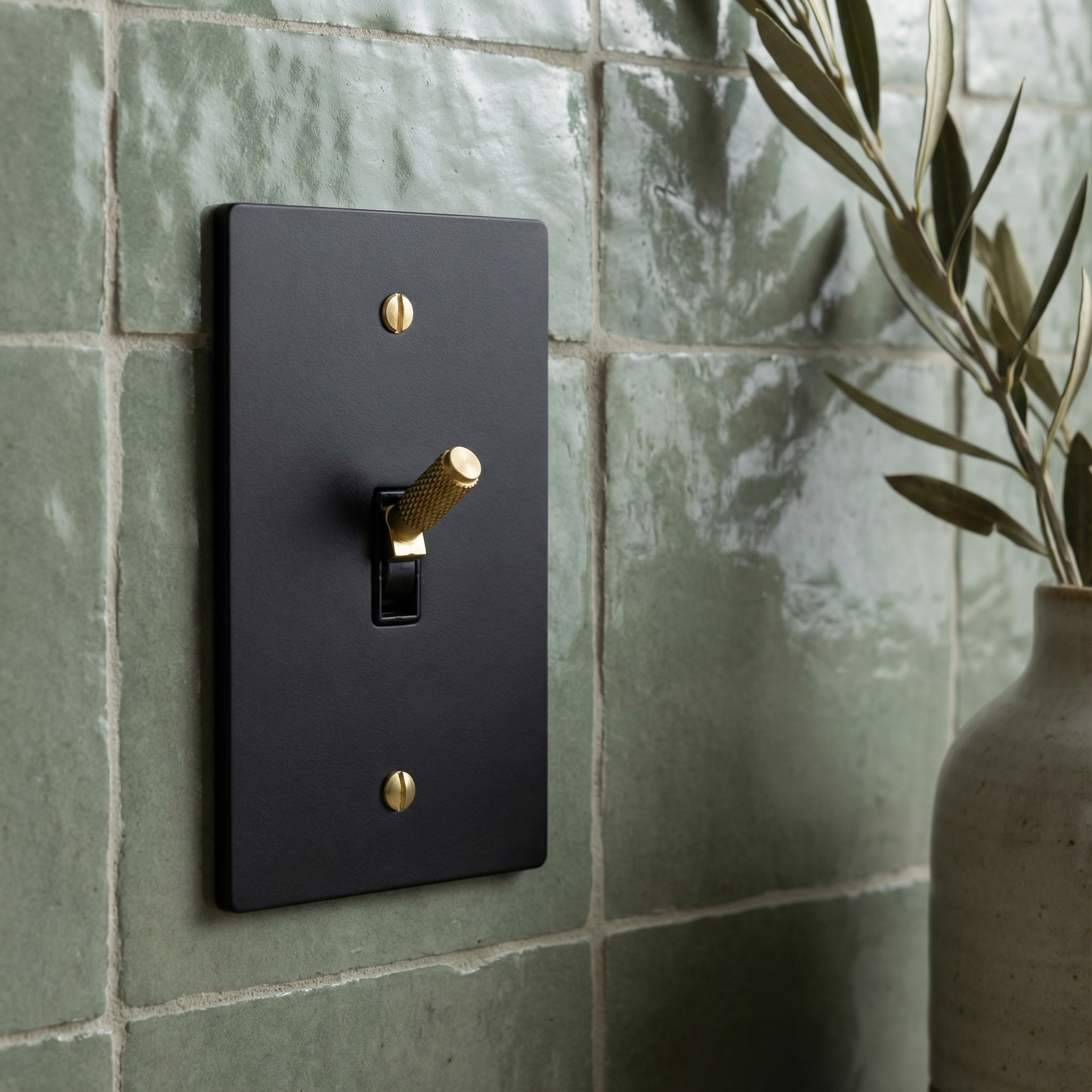 matte black (satin brass accents) 1 gang toggle switch plate on artisanal green tiles, evoking quiet luxury.
