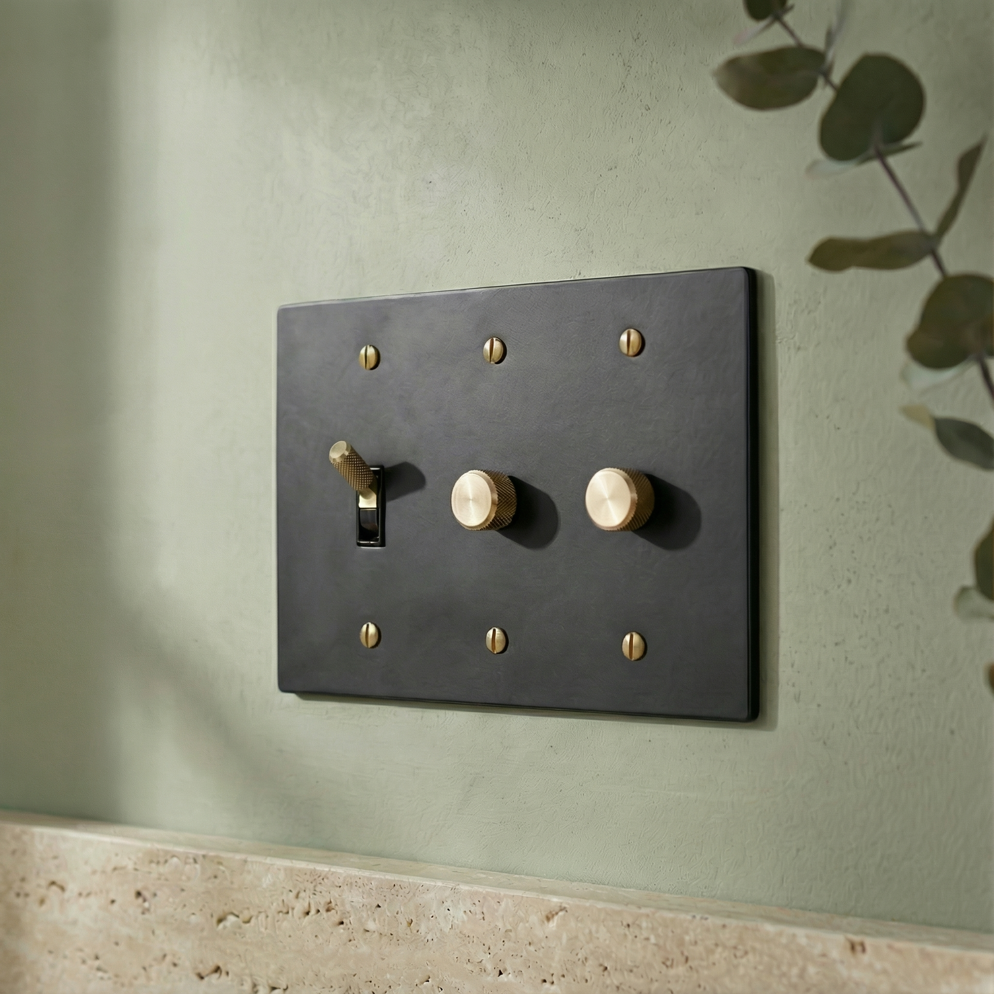 Elegant matte black (satin brass accents) 3 gang dimmer and toggle switch plate on a sage wall, evoking quiet luxury.