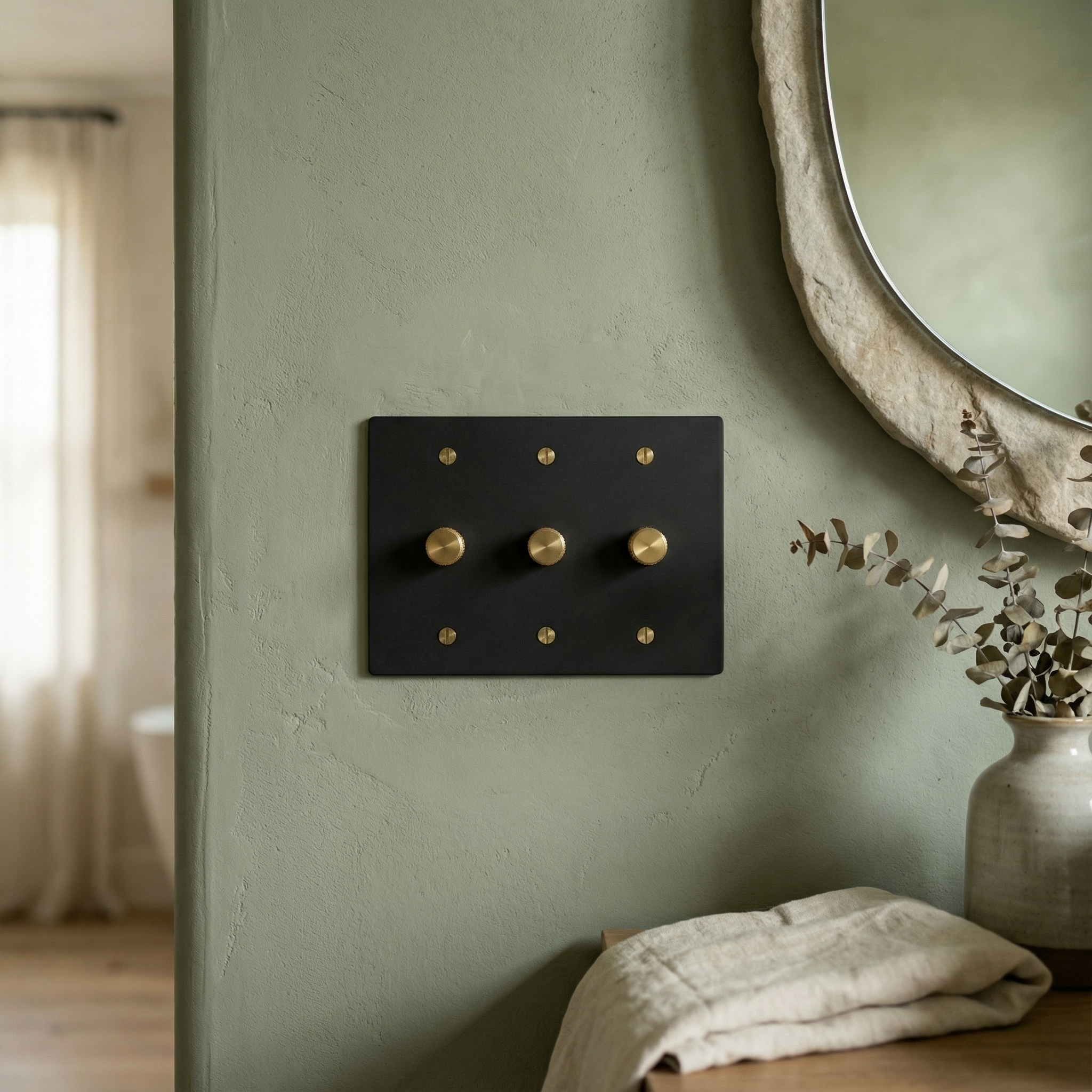 Elegant matte black (satin brass accents) 3 gang dimmer switch plate on a textured green wall, part of a quiet luxury setting.