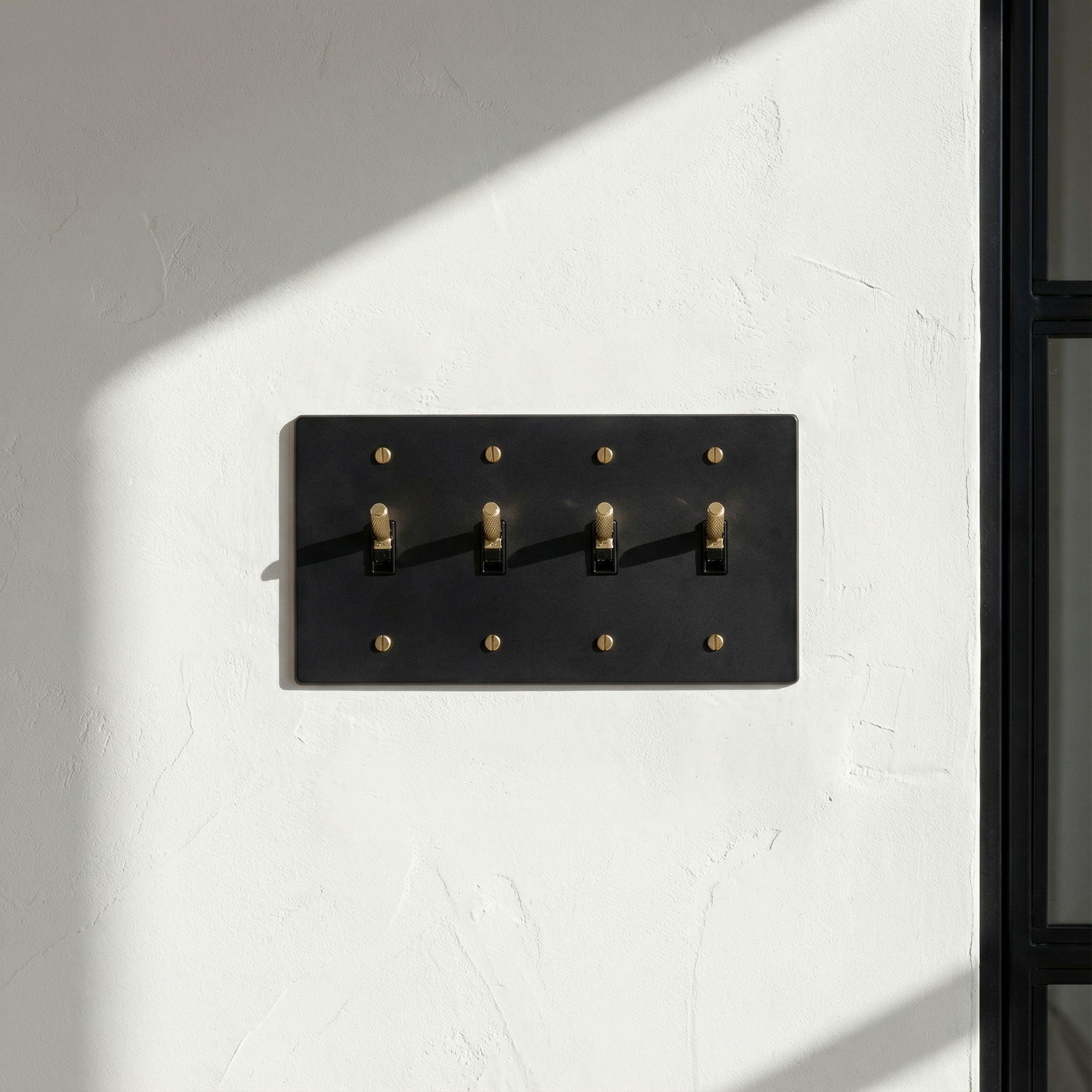 Matte black (satin brass accents) 4 gang toggle switch plate on a textured wall with sunlight and shadows, exuding timeless luxury.