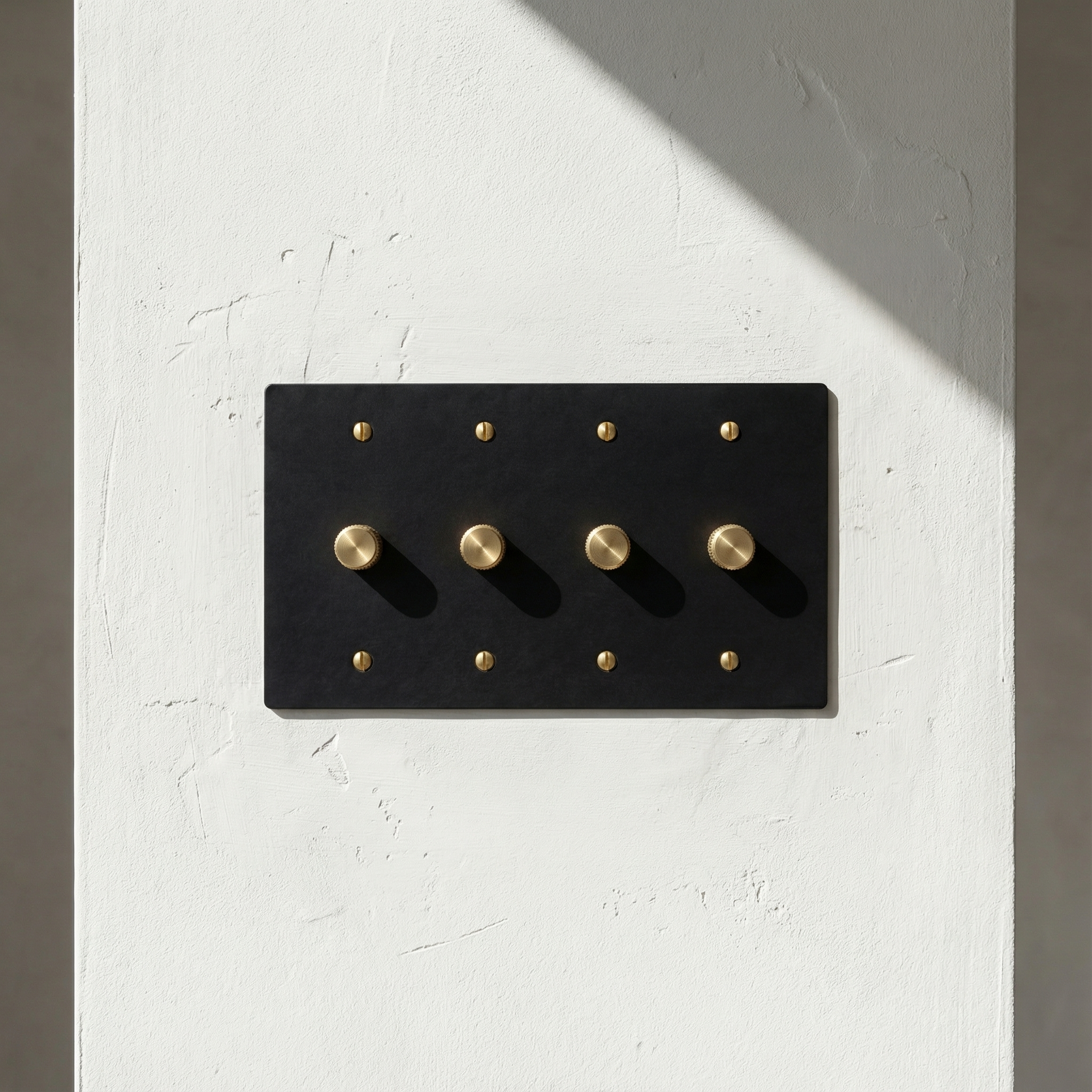 Elegant matte black (satin brass accents) 4 gang dimmer switch plate on a textured white wall, bathed in natural light, exuding quiet luxury.