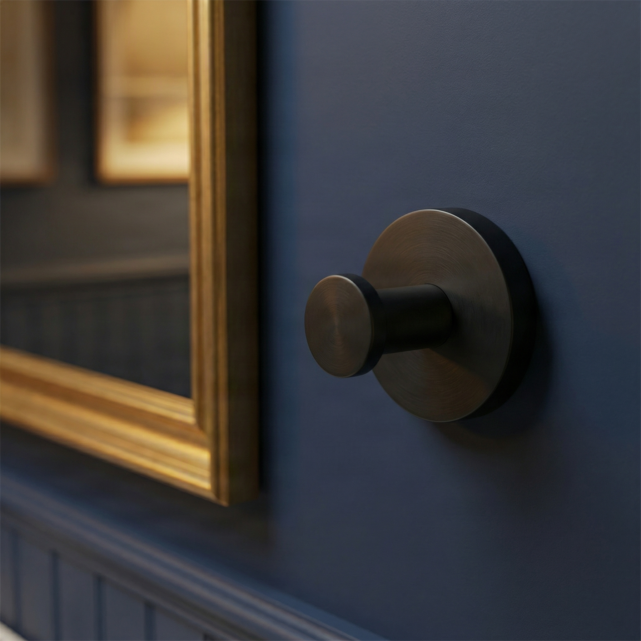 Modern brass bathroom hardware towel hook on a deep blue wall, beside a gold mirror, conveying timeless elegance.