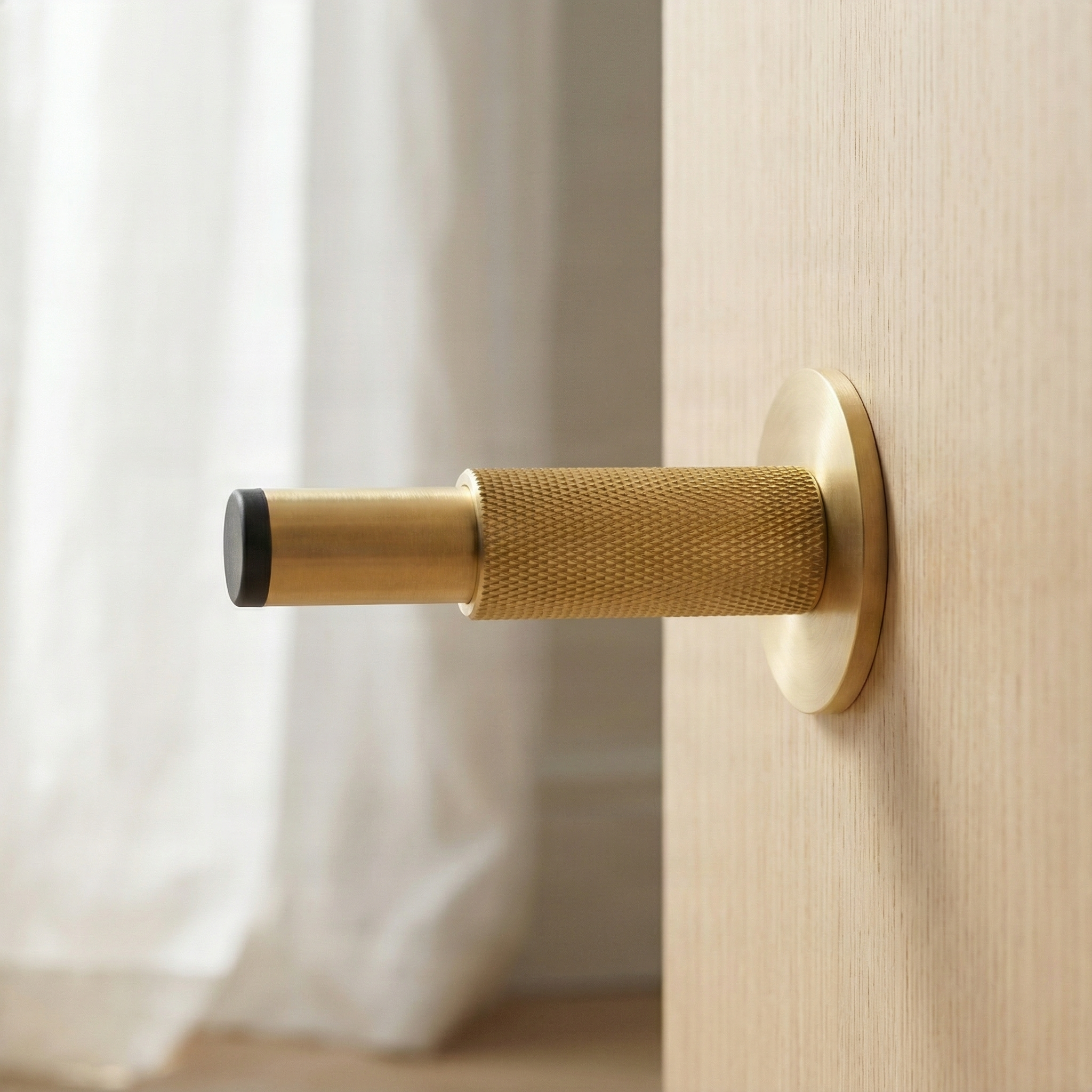 Knurled modern satin brass wall mount door stop on light wood, reflecting quiet, timeless luxury.