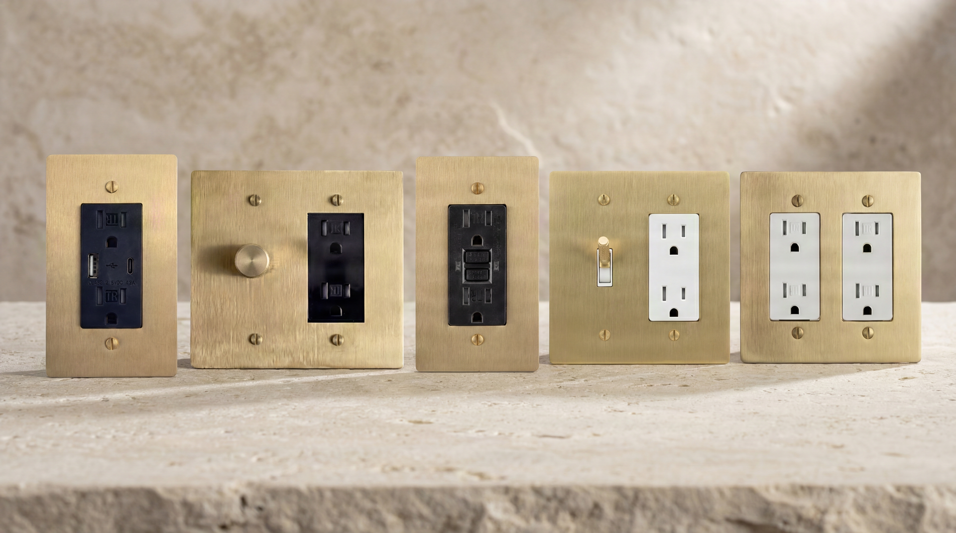 Five Satin Brass Outlets on textured stone: USB, rotary dimmer, GFCI, vintage toggle, duplex. Exquisite craftsmanship.