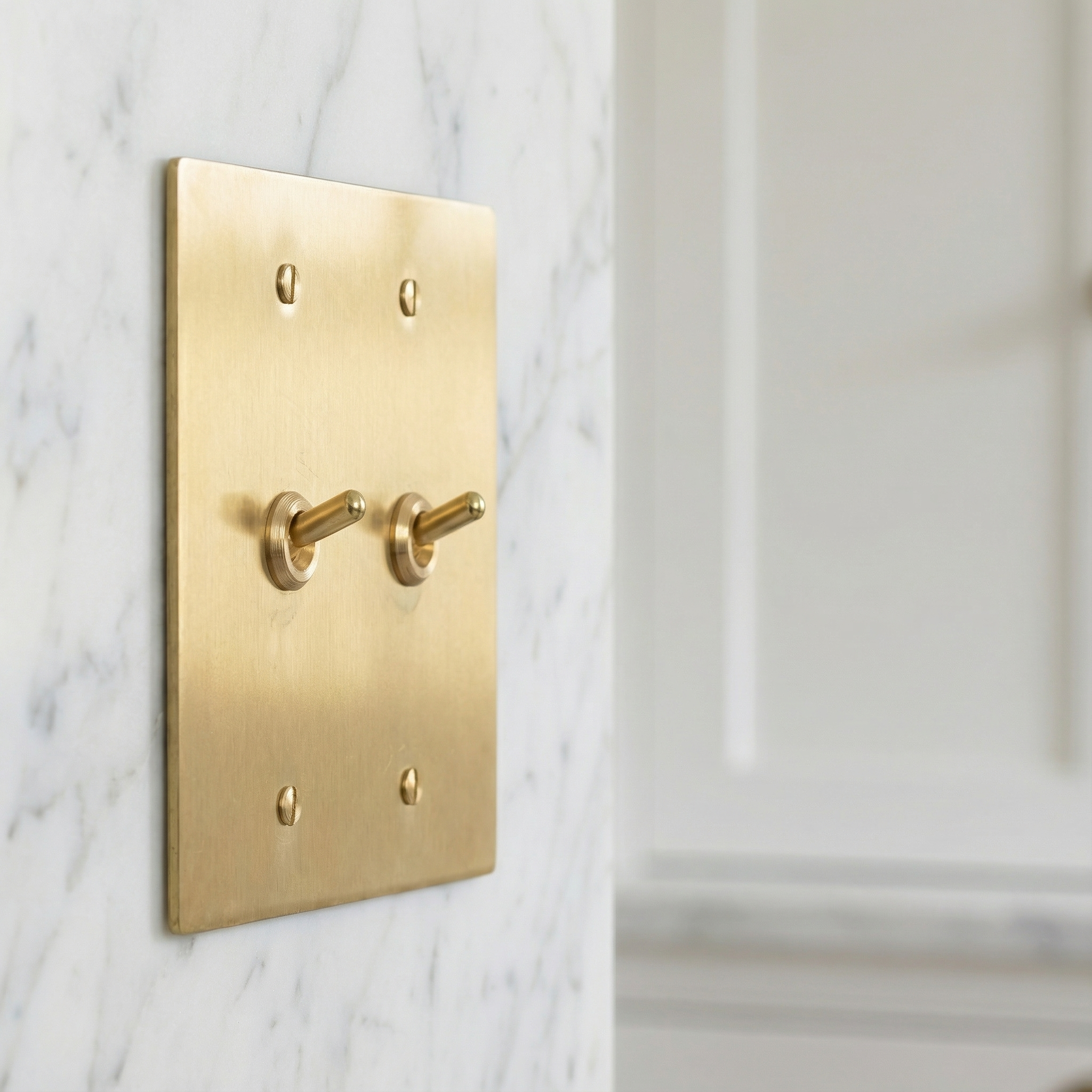 Satin brass 2 gang vintage toggle switch plate on a white marble wall, offering timeless elegance.