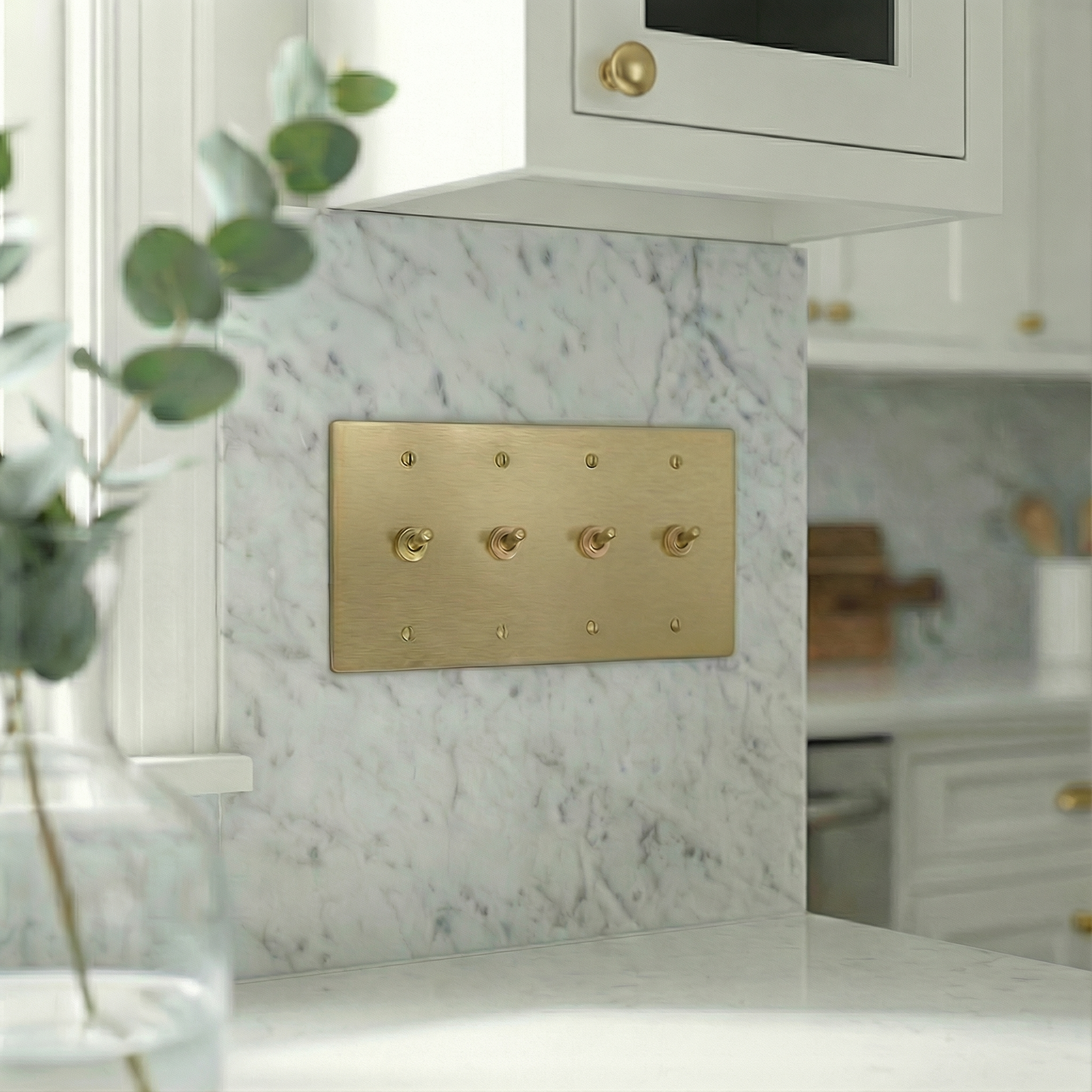 Satin brass 4 gang vintage toggle switch plate on white marble backsplash, adding timeless luxury to a kitchen.