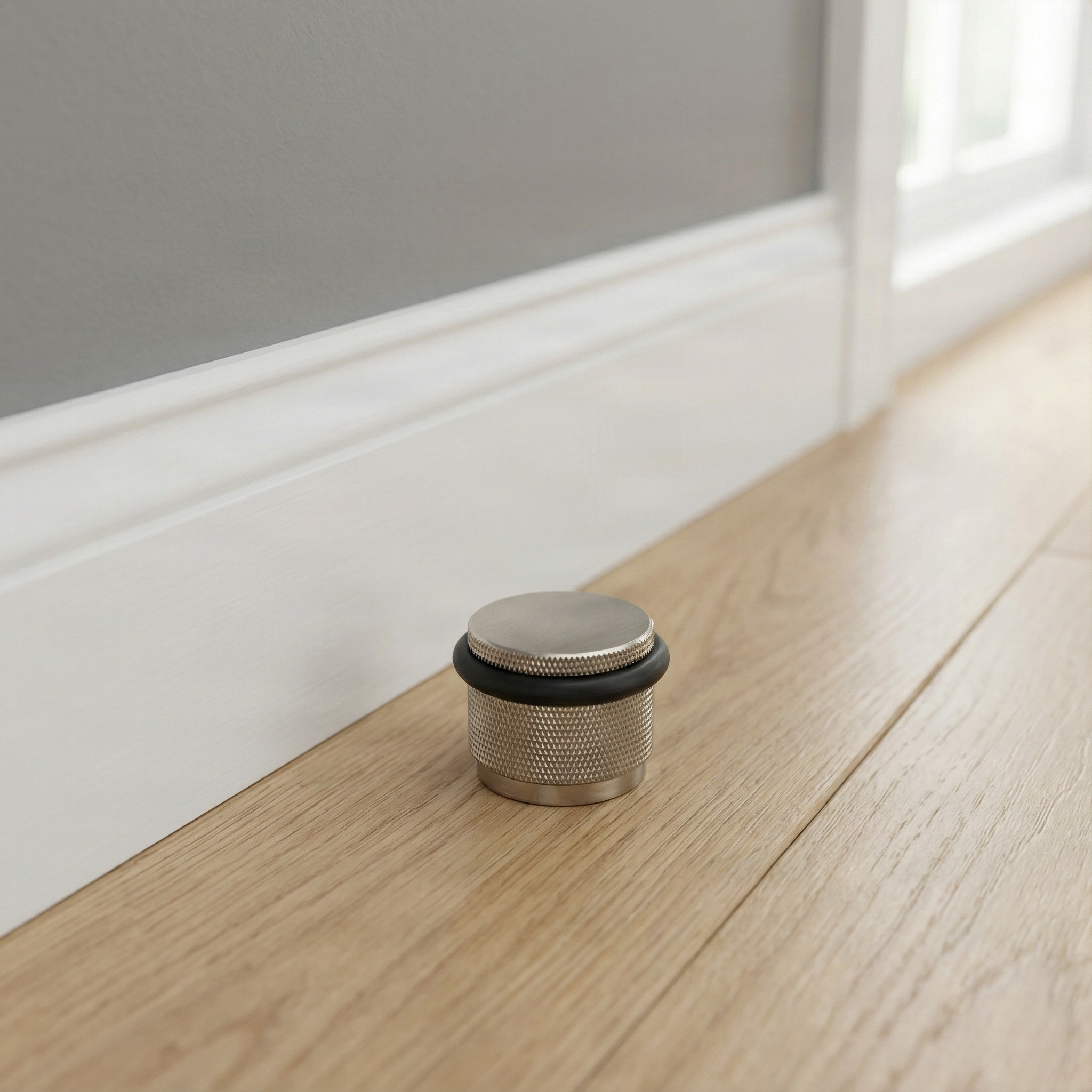 Knurled brass interior floor mount door stop on light wood floor, elegant grey wall.