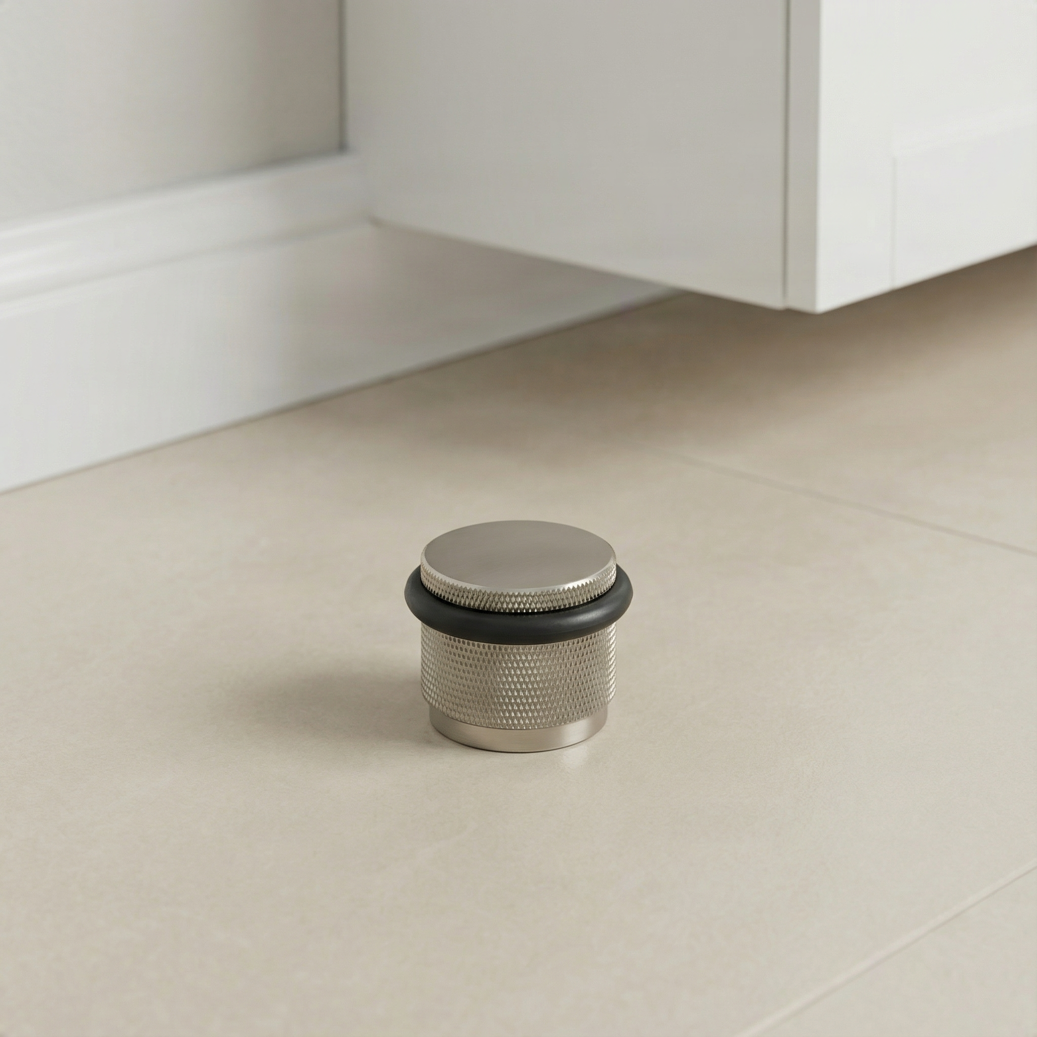 Refined knurled satin nickel floor mount door stop on light tile in an elegant room setting.