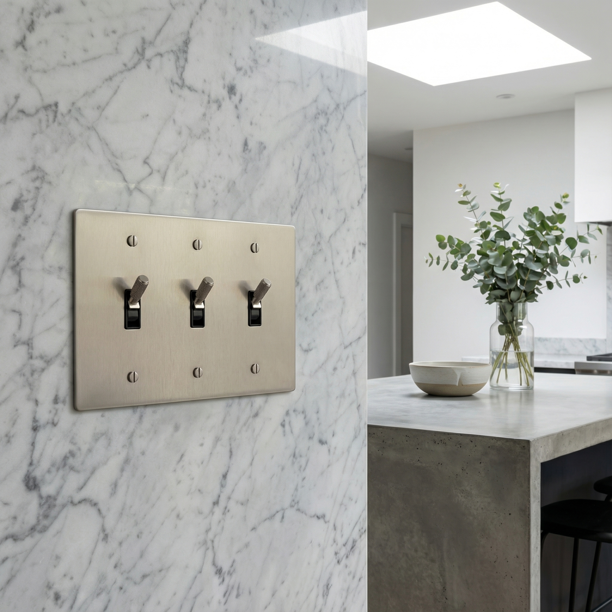 A satin nickel 3 gang toggle switch plate on a marble wall, exuding quiet luxury in a modern, timeless kitchen.